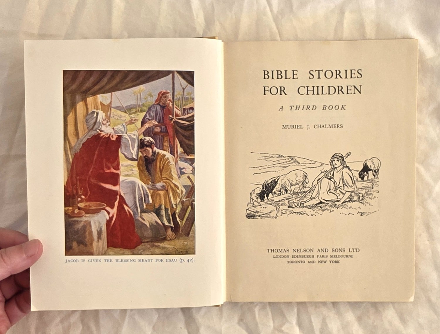 Open book titled 'Bible Stories for Children: A Third Book' held by a hand on a textured surface.