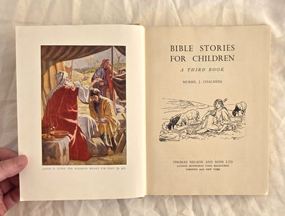 Open book titled 'Bible Stories for Children: A Third Book' held by a hand on a textured surface.
