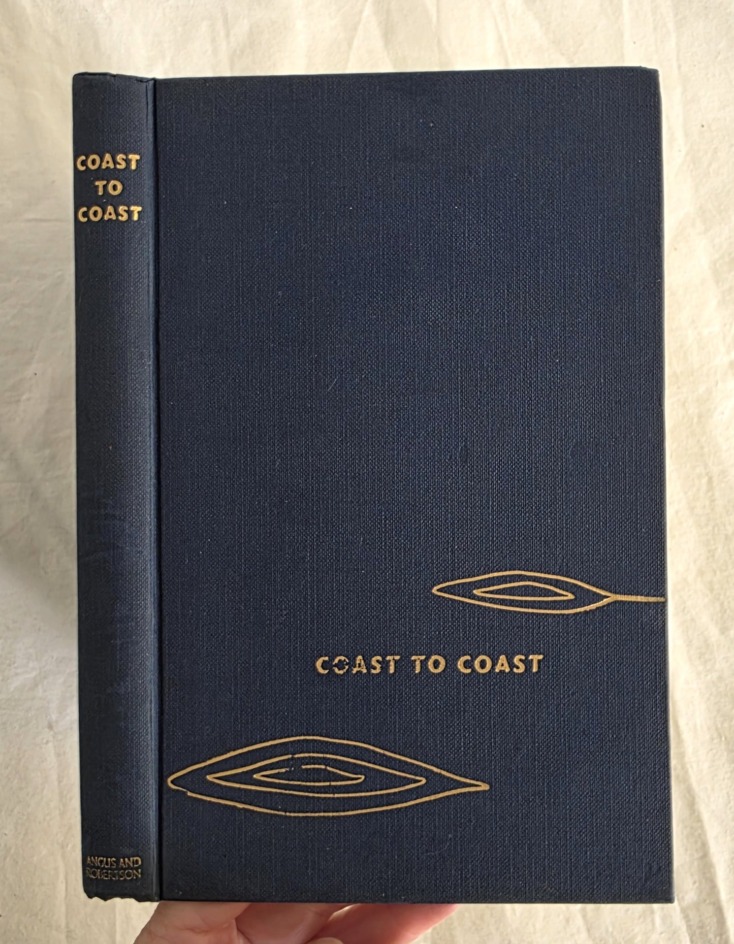 Blue book titled 'Coast to Coast' with gold text and design on a beige background