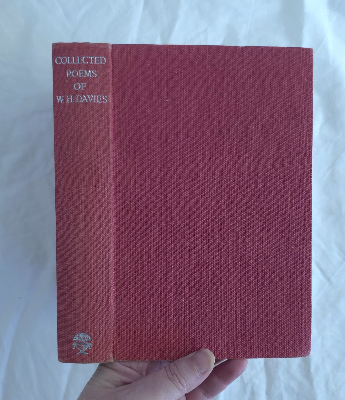 Red book titled 'Collected Poems of W.H. Davies' held by a hand on a white background