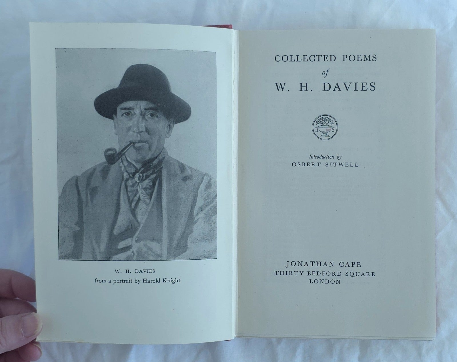 Open book titled 'Collected Poems of W. H. Davies' held by a hand on a white background