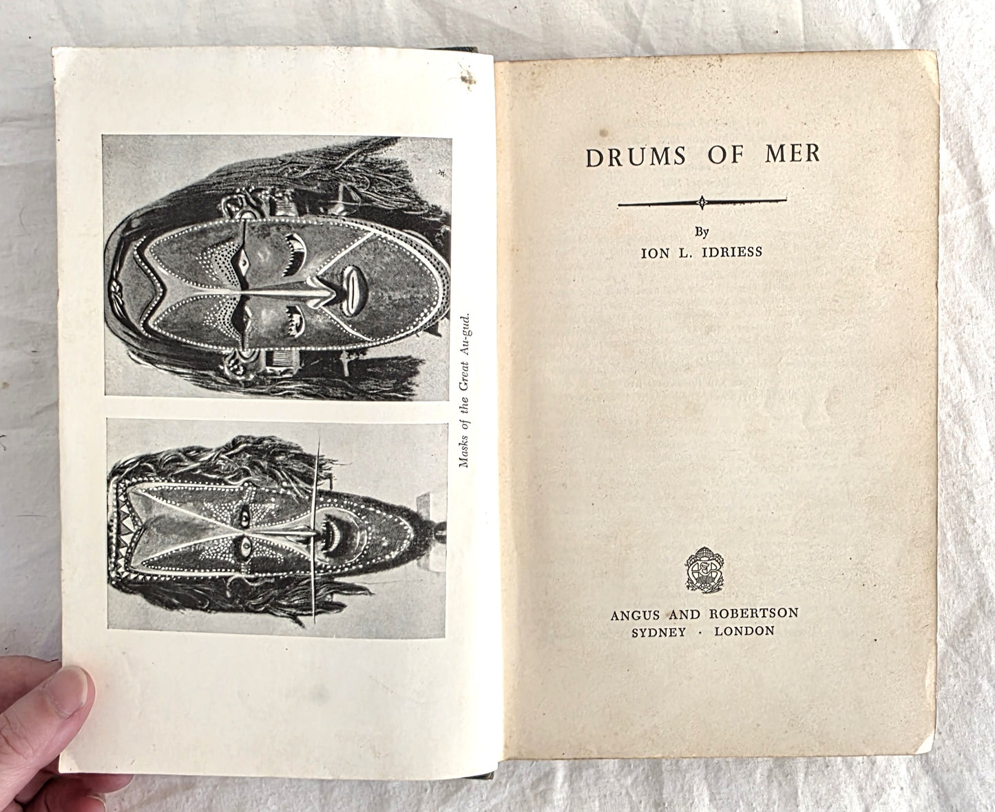 Open book titled 'Drums of Mer' by Ion L. Idriess with illustrations on a white background