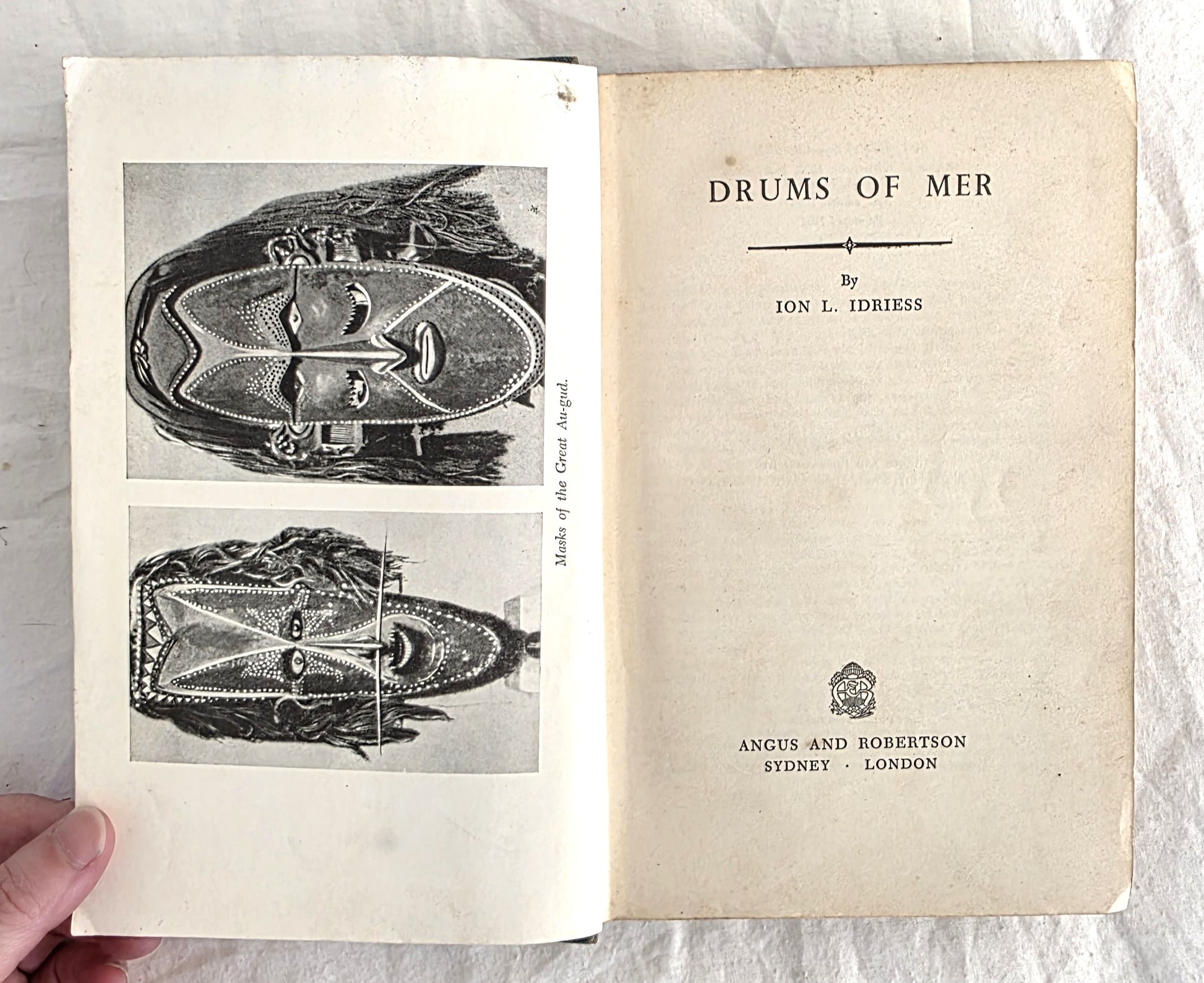 Open book titled 'Drums of Mer' by Ion L. Idriess with illustrations on a white background