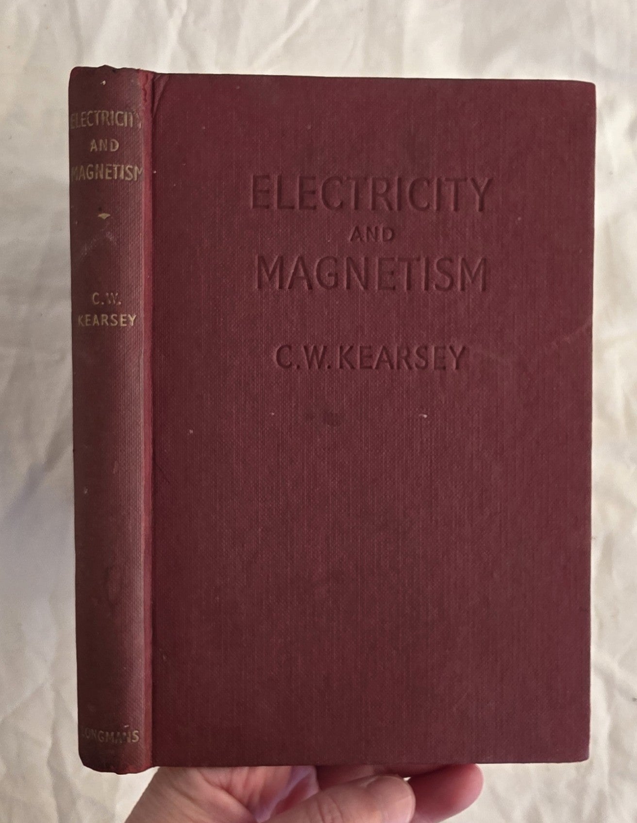 Maroon book titled 'Electricity and Magnetism' by C.W. Kearsey held against a light background