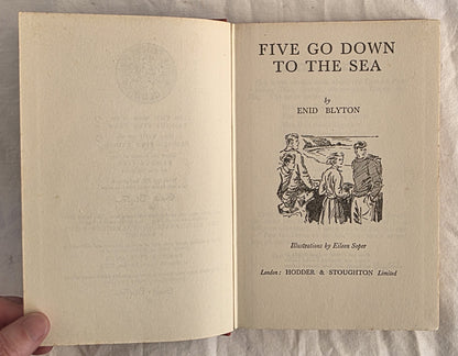 Open book titled 'Five Go Down to the Sea' by Enid Blyton with illustrations on a textured surface.