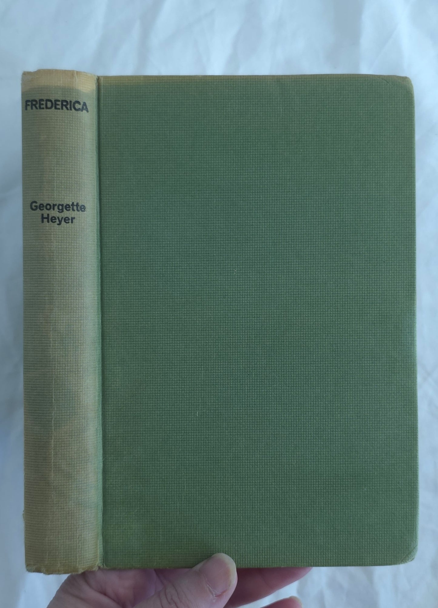 Green book with yellowed spine held by a hand on a white background