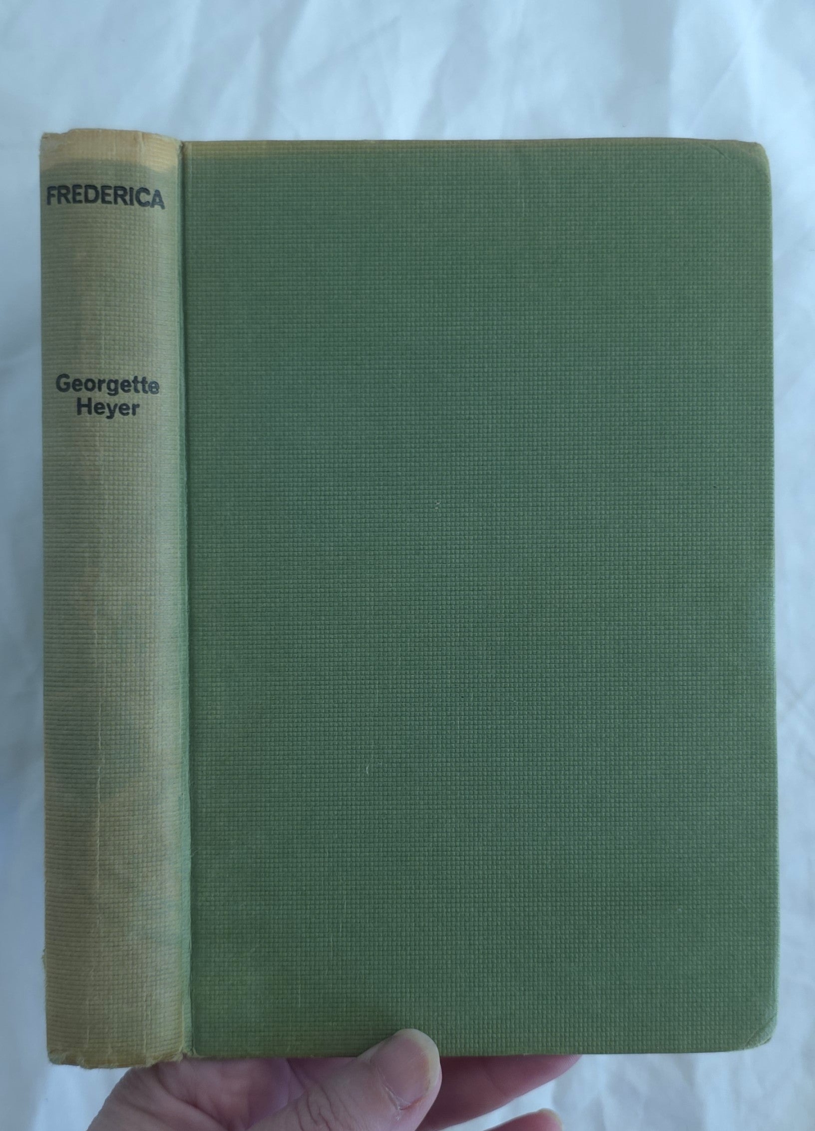 Green book with yellowed spine held by a hand on a white background