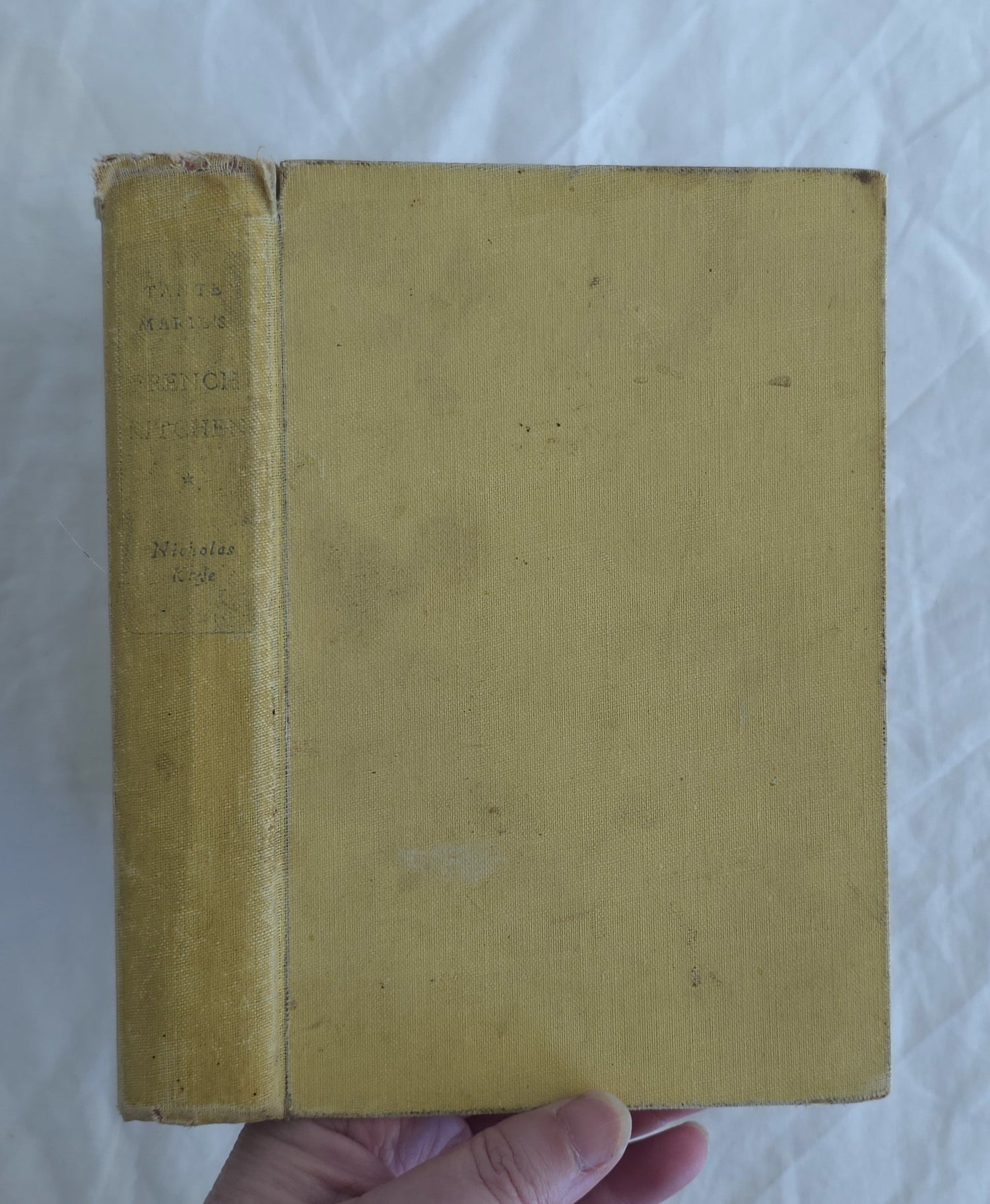 Yellowed book cover held by a hand on a white background