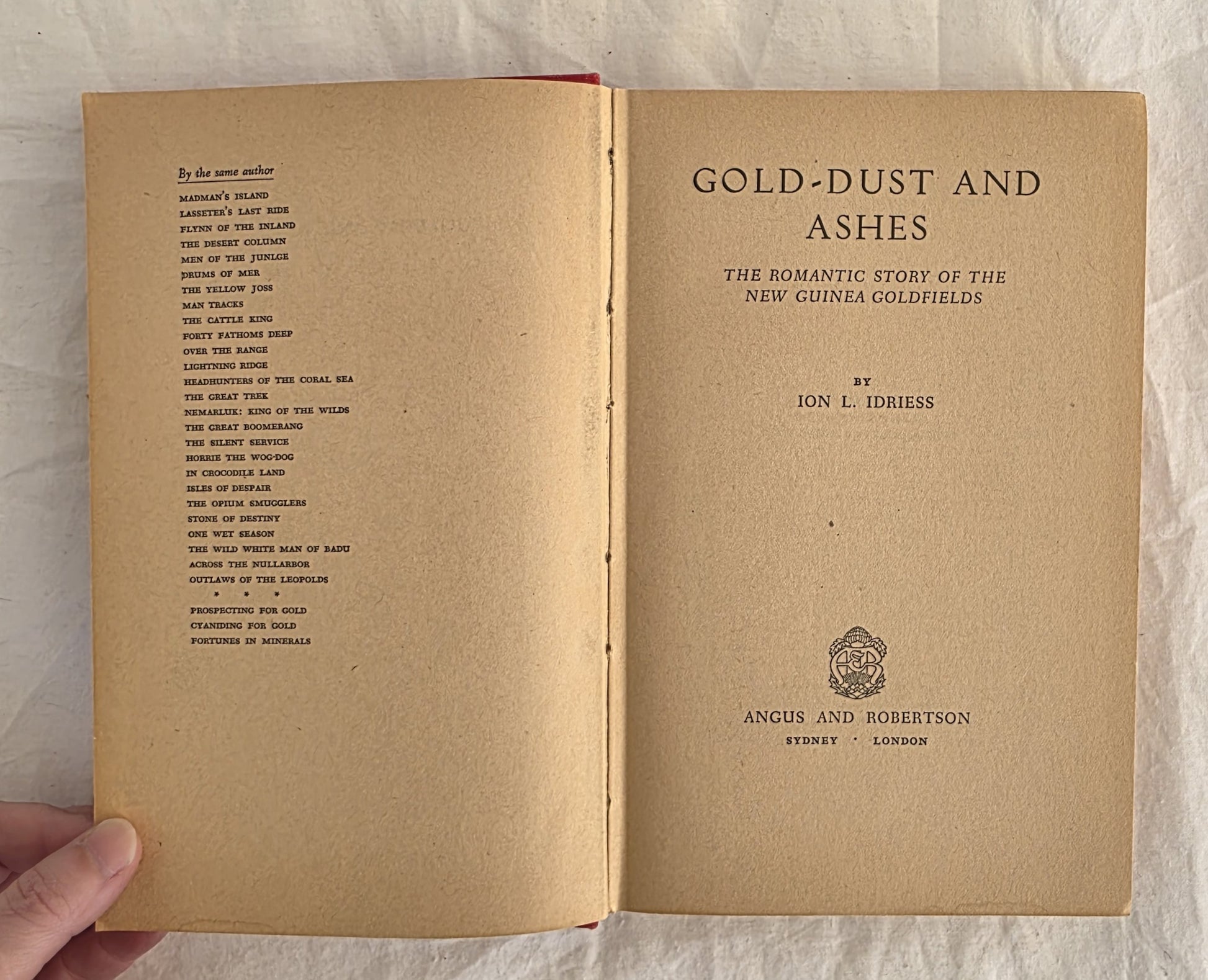 Open book titled 'Gold-Dust and Ashes' by Jon L. Idiess on a textured surface.