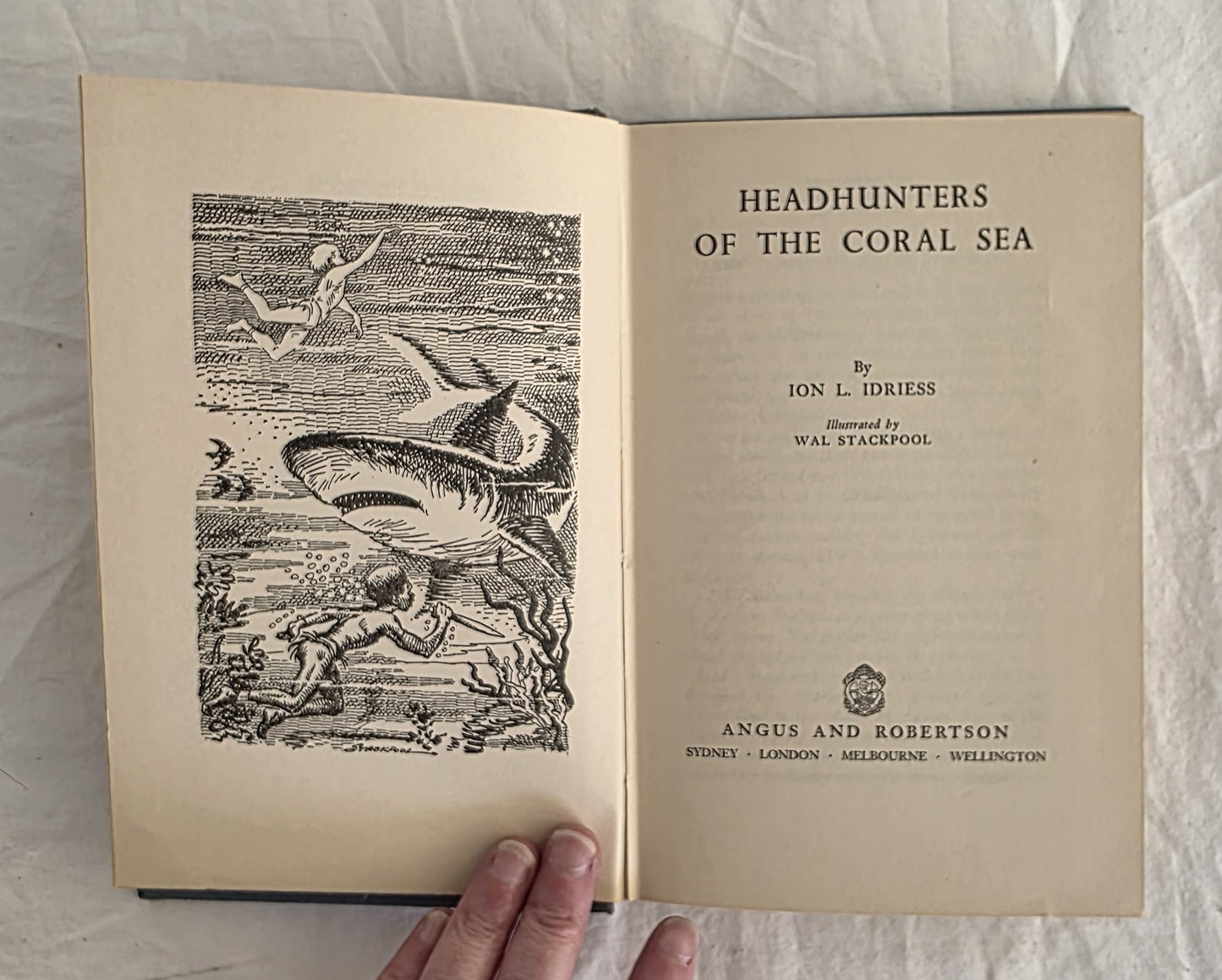 Open book titled 'Headhunters of the Coral Sea' with a shark illustration on a textured surface.