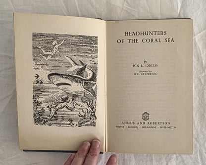 Open book titled 'Headhunters of the Coral Sea' with a shark illustration on a textured surface.