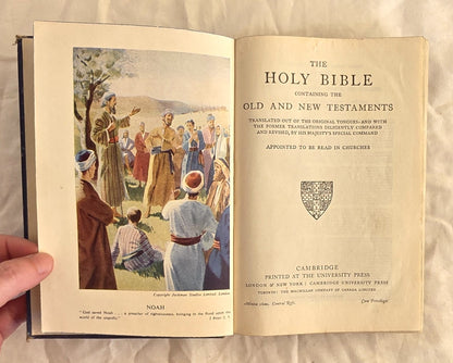 Open book showing a biblical scene with people and trees, held by a hand.