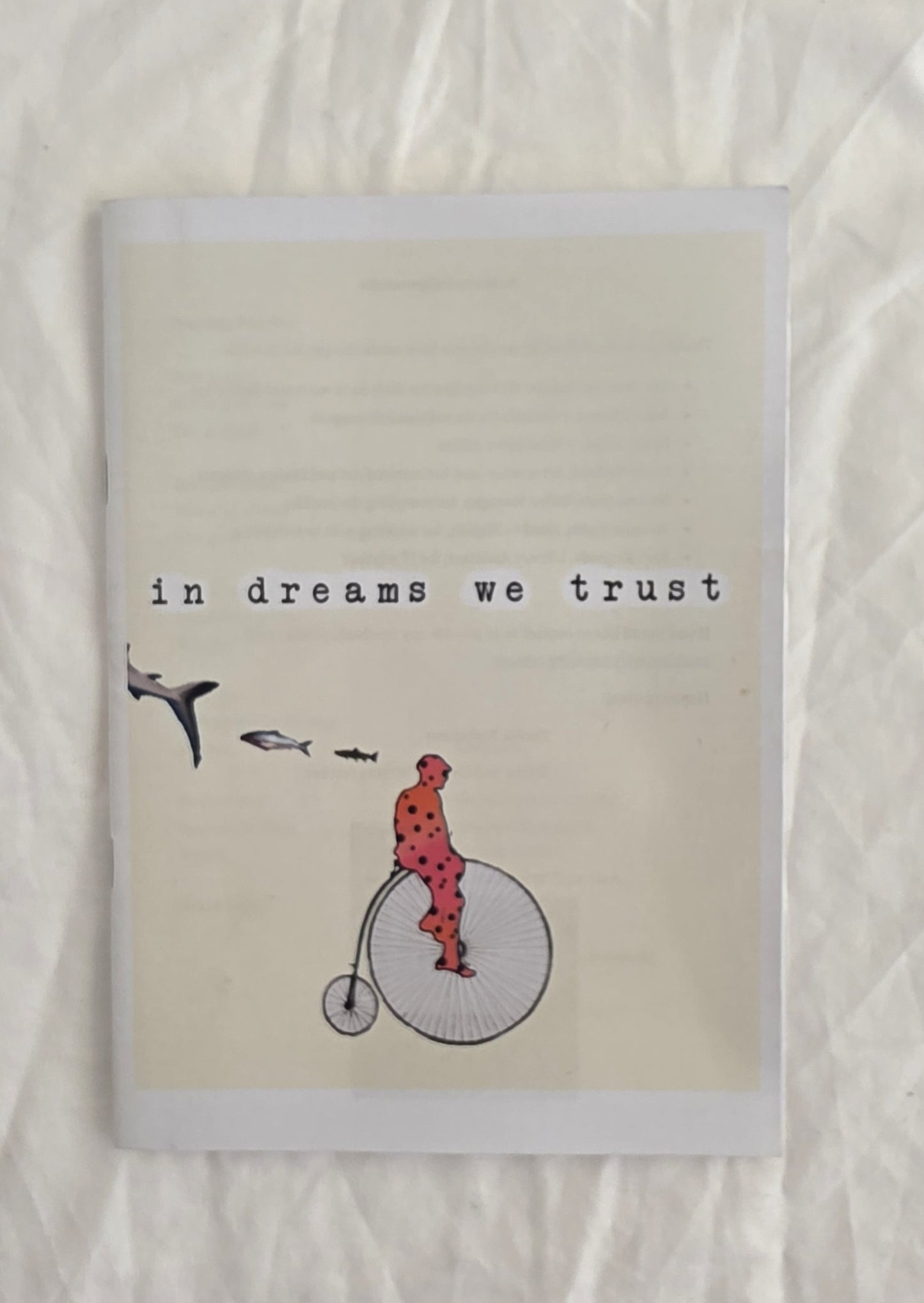 Notebook with illustration of a person on a penny farthing bicycle and text 'in dreams we trust' on a textured beige background.