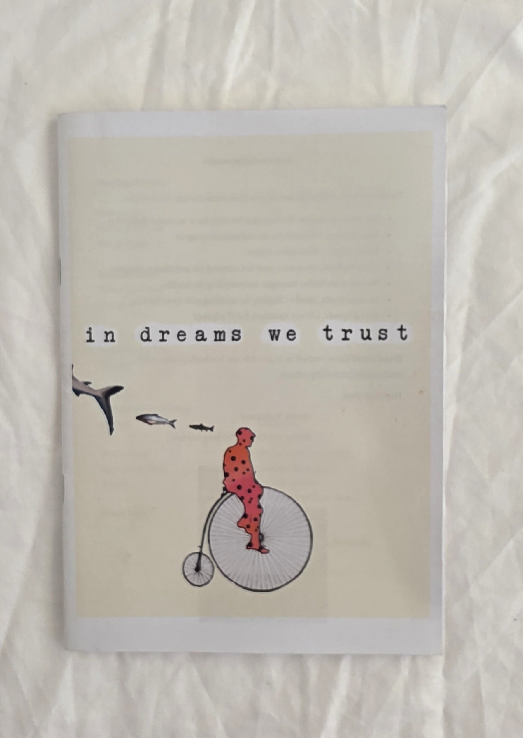 Notebook with illustration of a person on a penny farthing bicycle and text 'in dreams we trust' on a textured beige background.