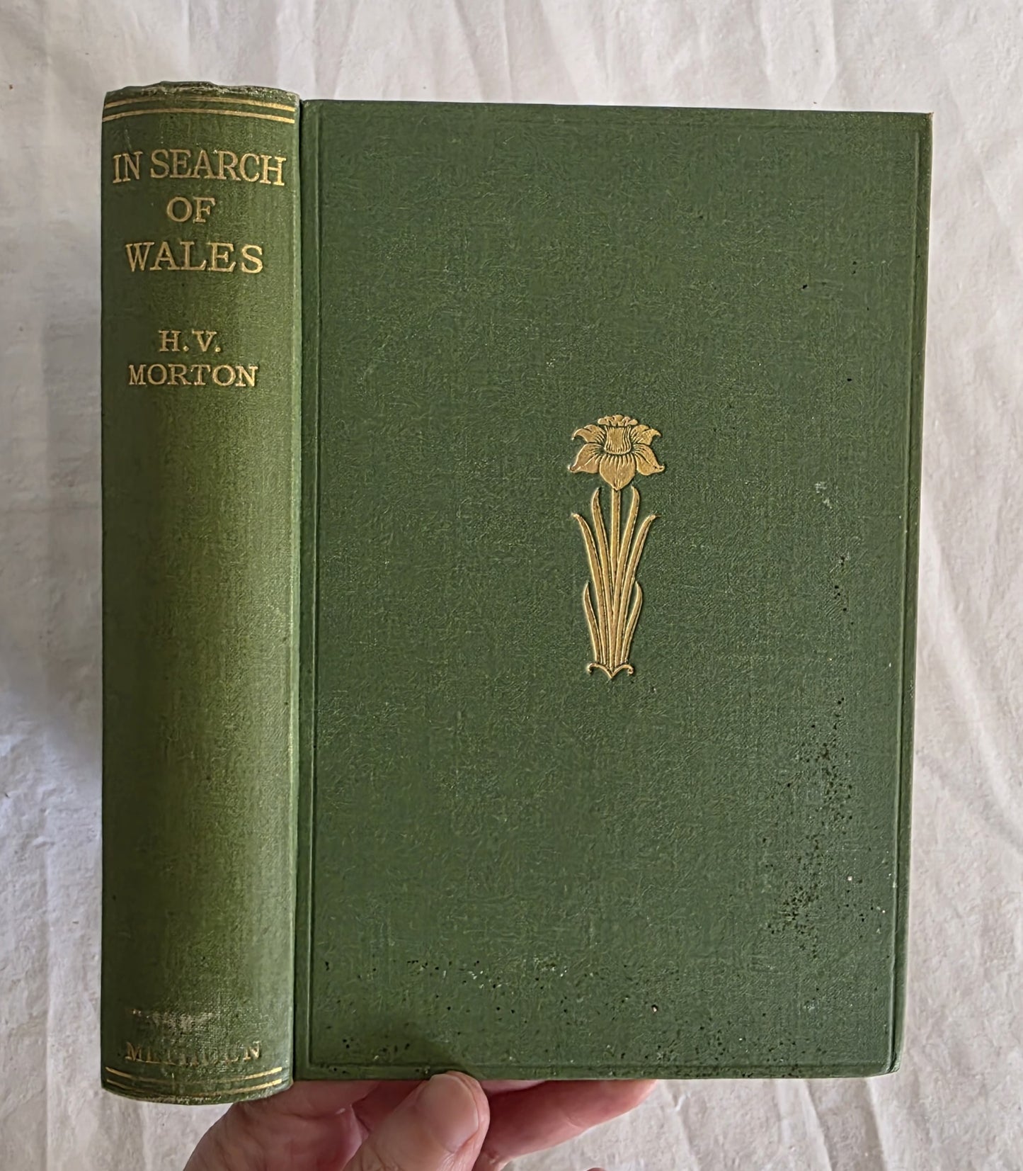 Green book titled 'In Search of Wales' by H.V. Morton with a floral emblem on a light gray background