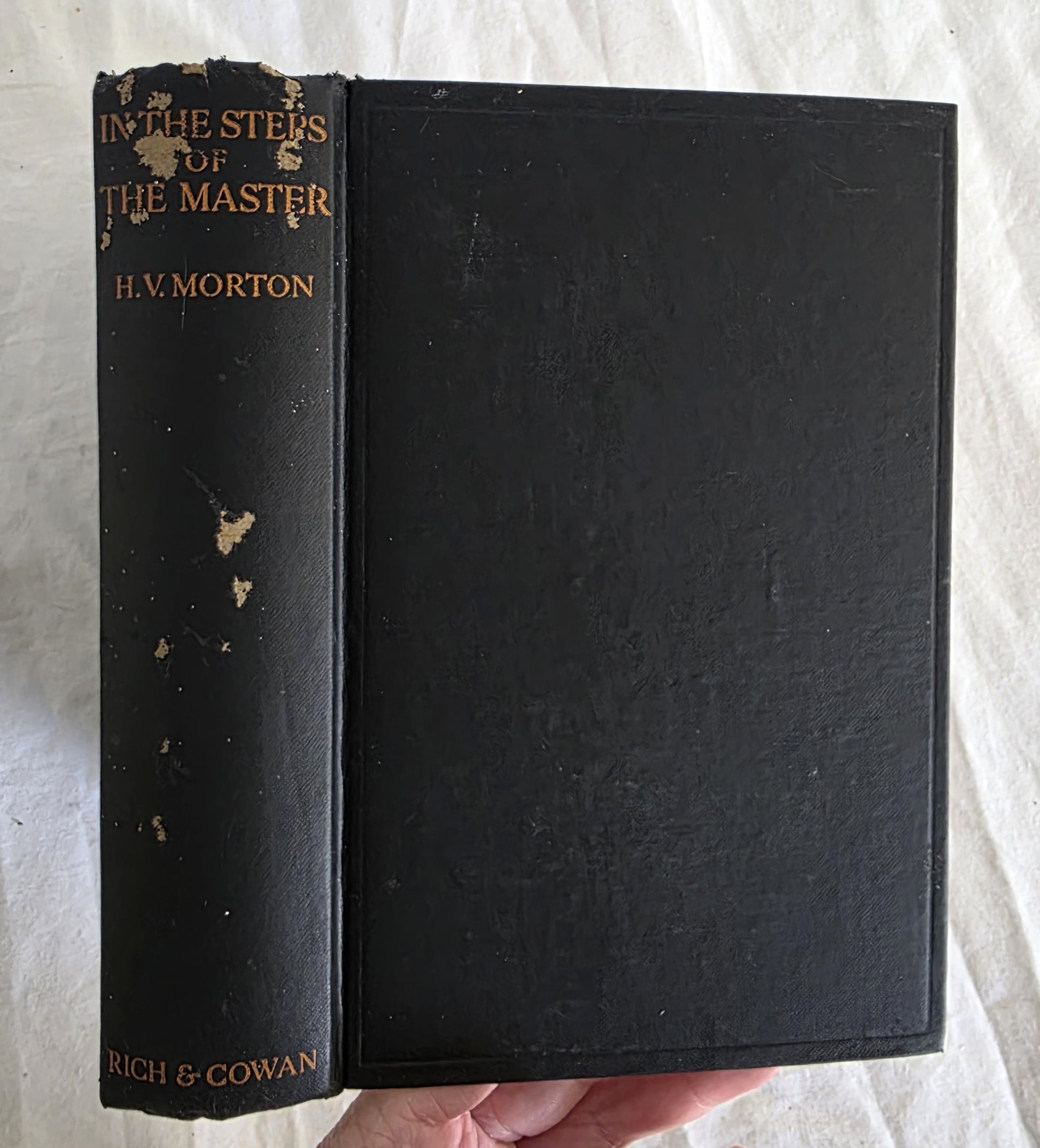 Vintage black book titled 'In the Steps of the Master' by H.V. Morton, held against a white fabric background.
