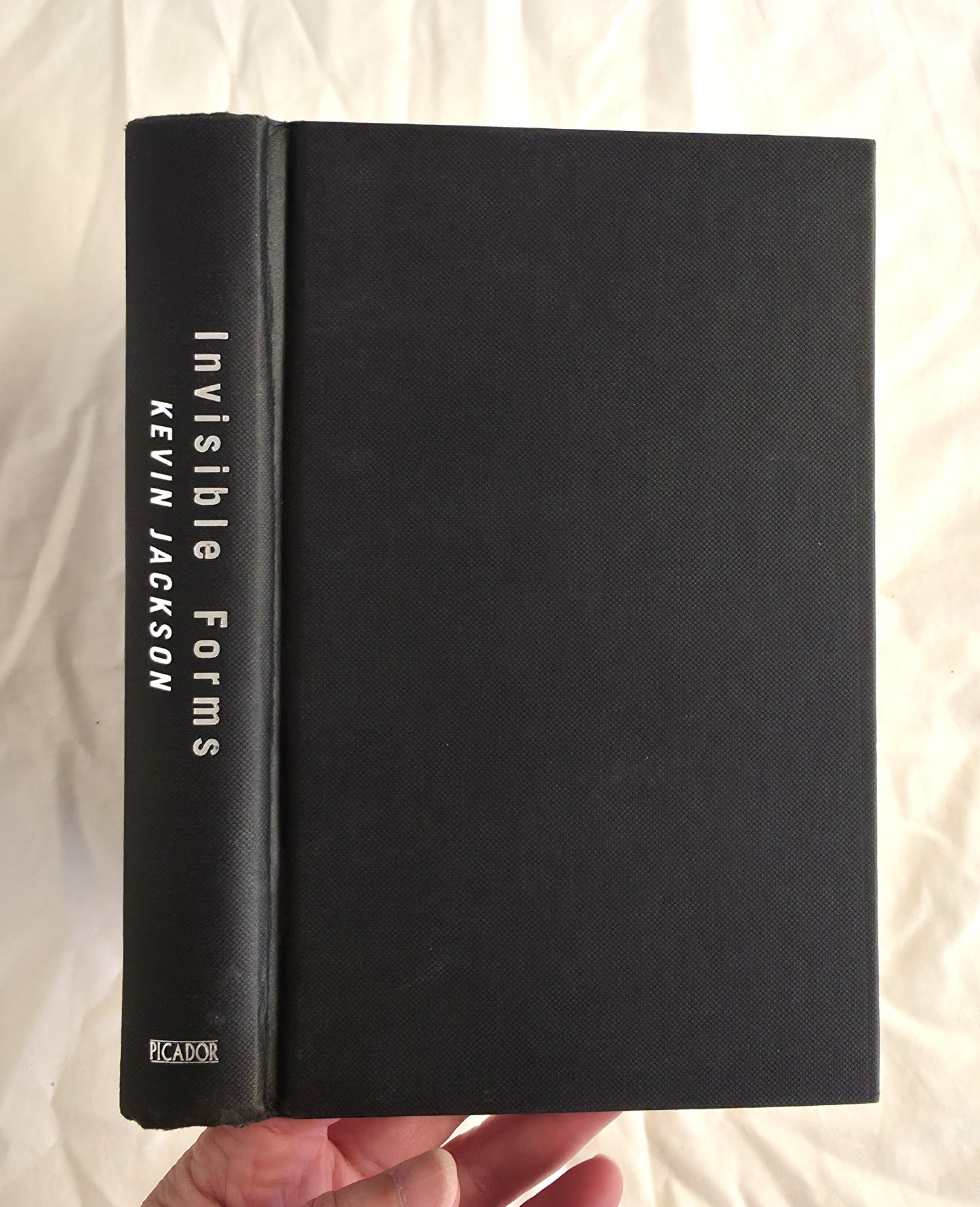 Black book titled 'Invisible Forms' by Kevin Jackson held against a light background