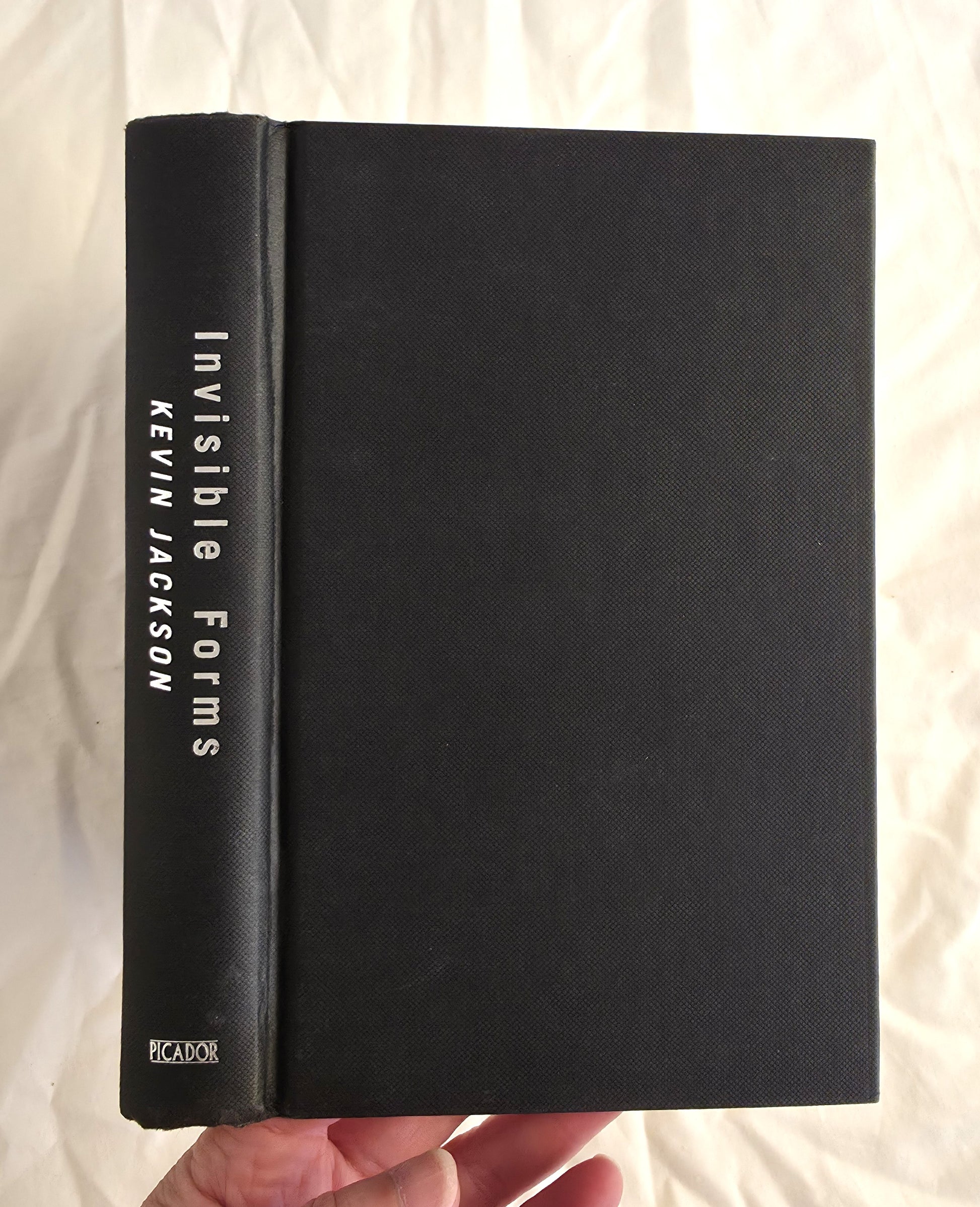 Black book titled 'Invisible Forms' by Kevin Jackson held against a light background