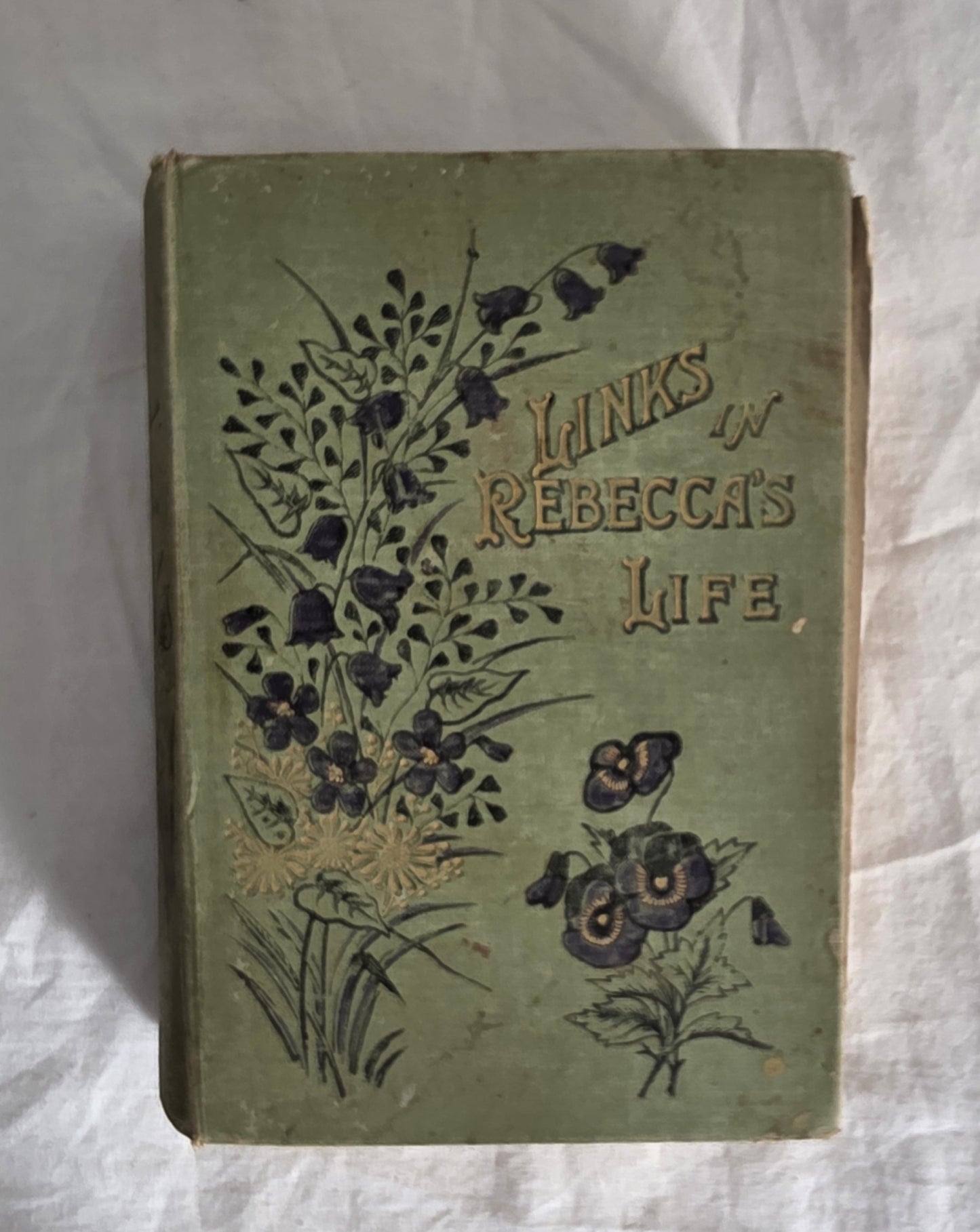 Vintage book titled 'Links in Rebecca's Life' with floral design on a white fabric background