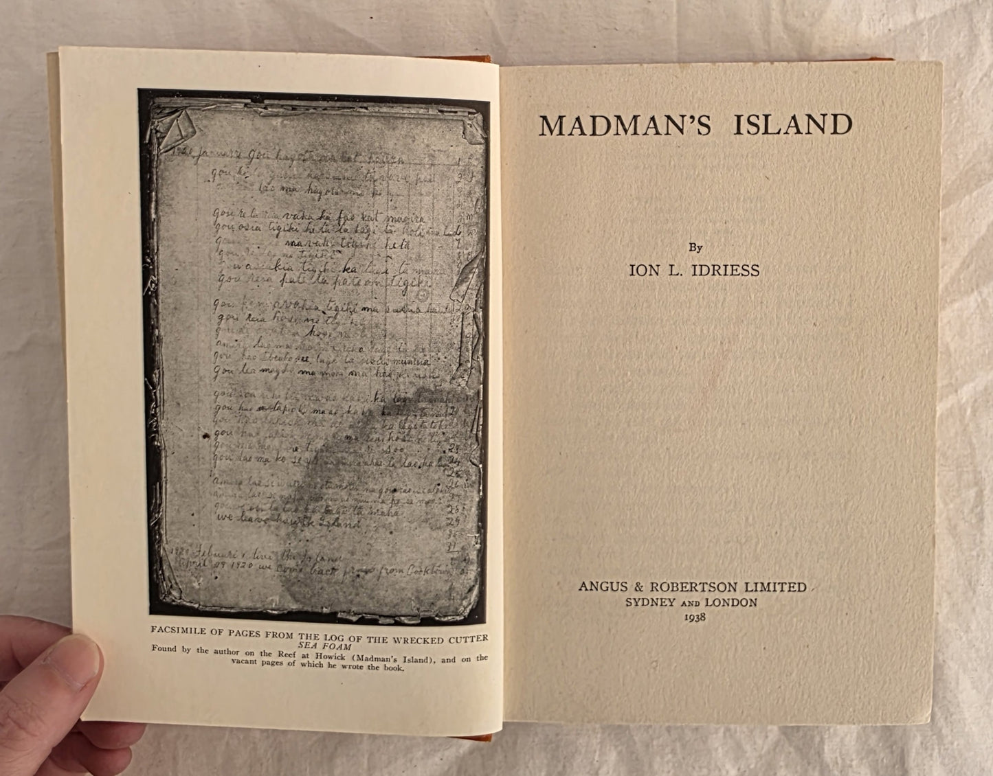 Open book titled 'Madman's Island' by Ion L. Idriess on a textured surface.