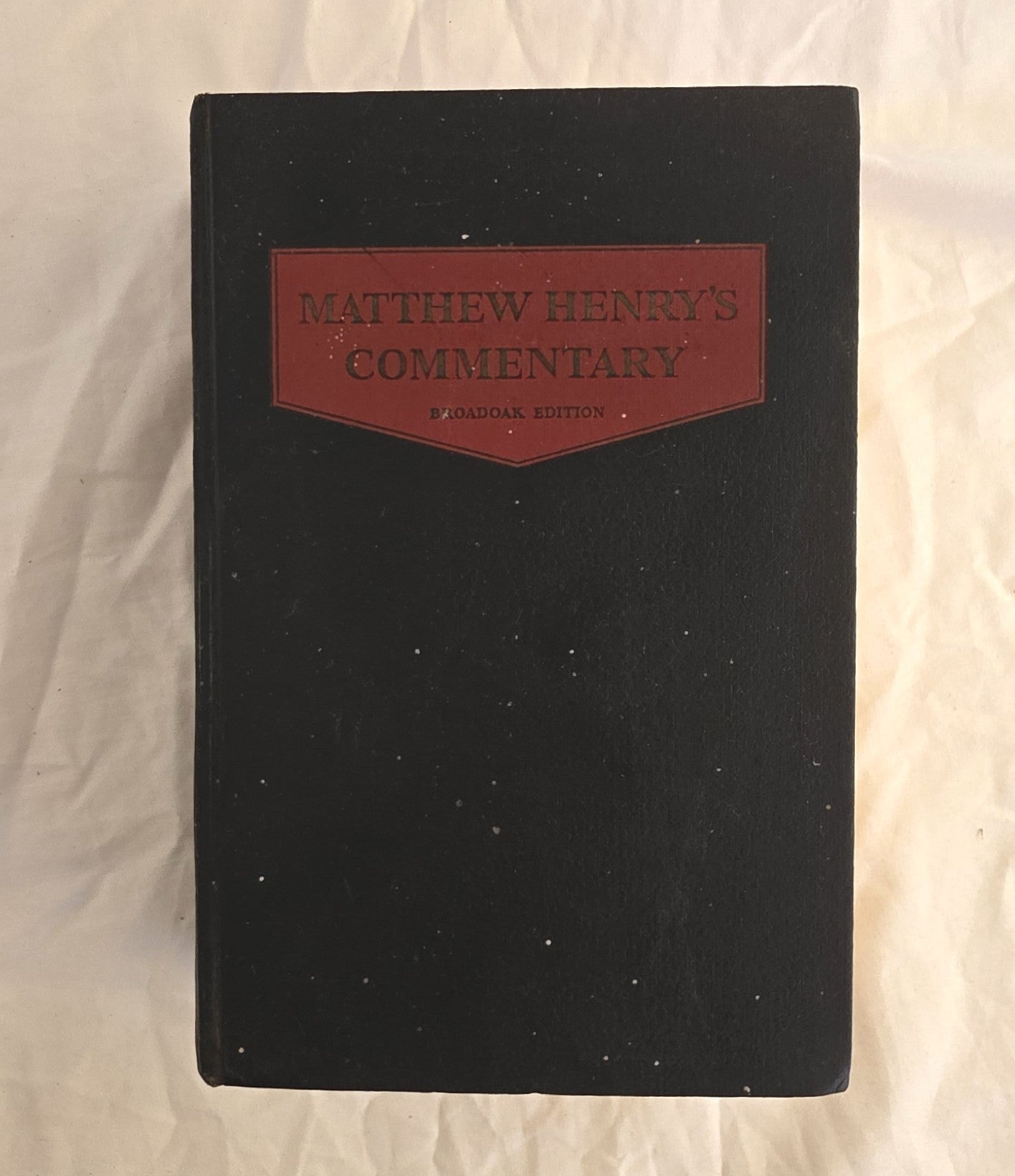 Black book with a red leather patch labeled 'Matthew Henry's Commentary' on a textured beige background