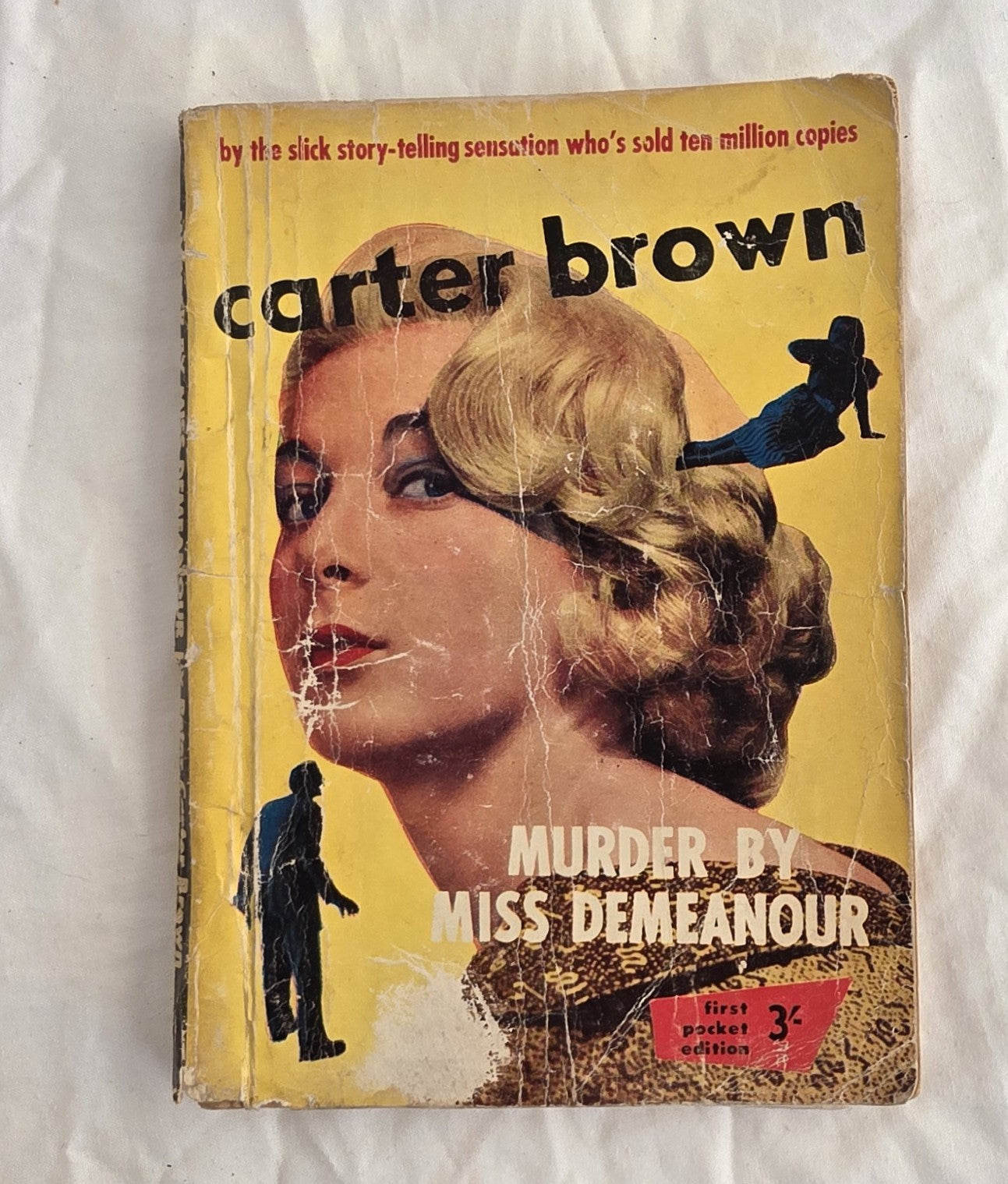 Vintage book cover with a woman's face and text about Carter Brown's 'Murder by Miss Demeanor' on a white background.