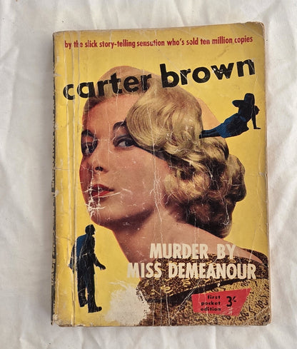 Vintage book cover with a woman's face and text about Carter Brown's 'Murder by Miss Demeanor' on a white background.