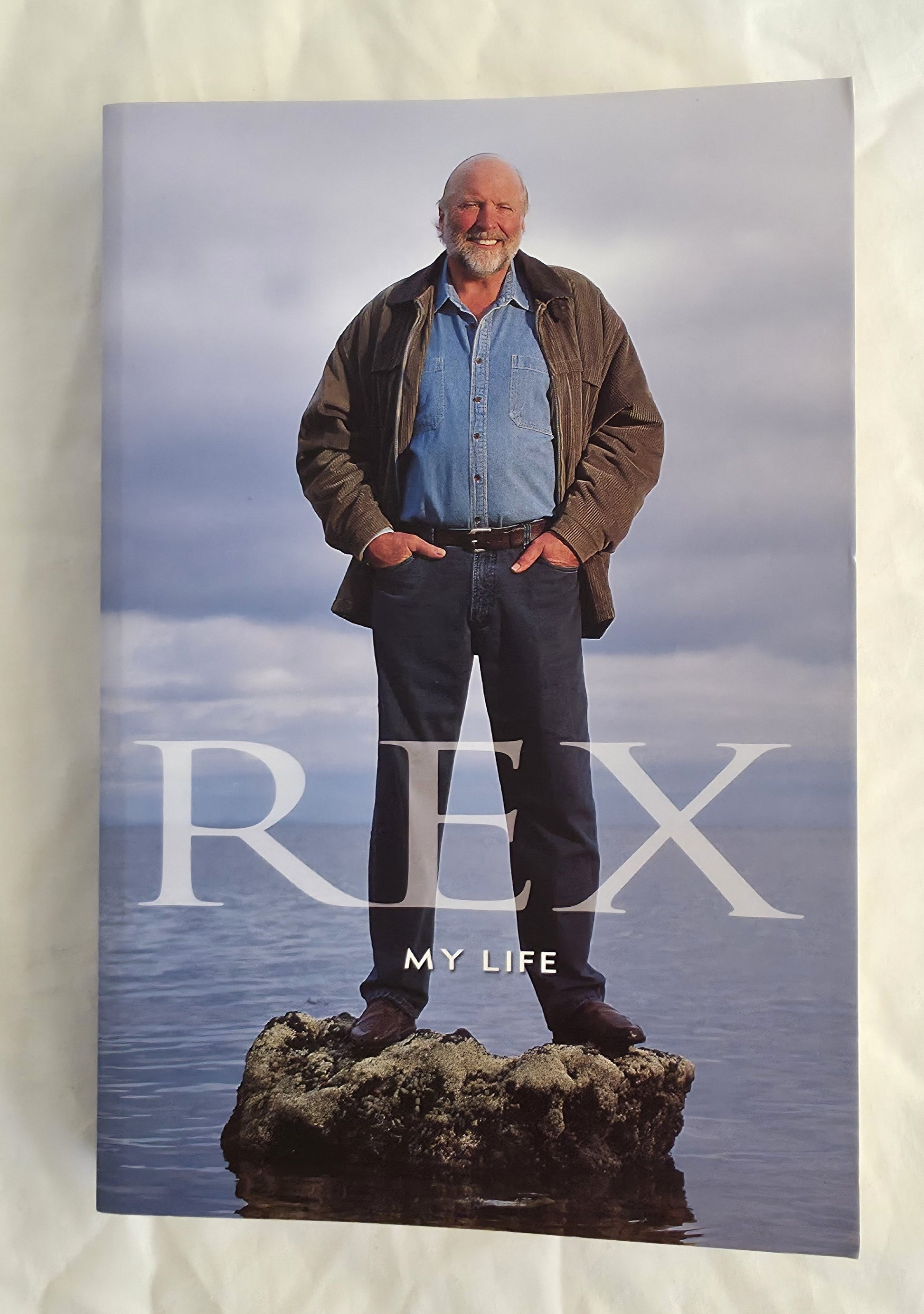 Book cover titled 'Rex My Life' featuring a person standing on a rock with water in the background.