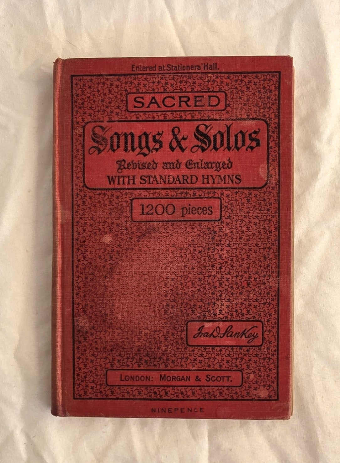 Red book titled 'Sacred Songs & Solos' on a textured beige background