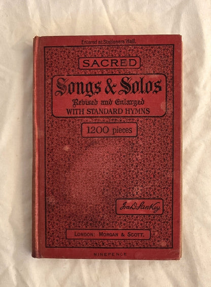 Red book titled 'Sacred Songs & Solos' on a textured beige background