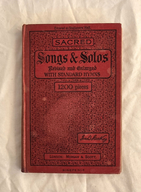 Red book titled 'Sacred Songs & Solos' on a textured beige background