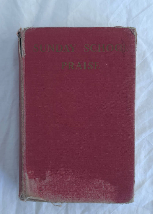 Red book titled 'Sunday School Praise' on a white textured surface