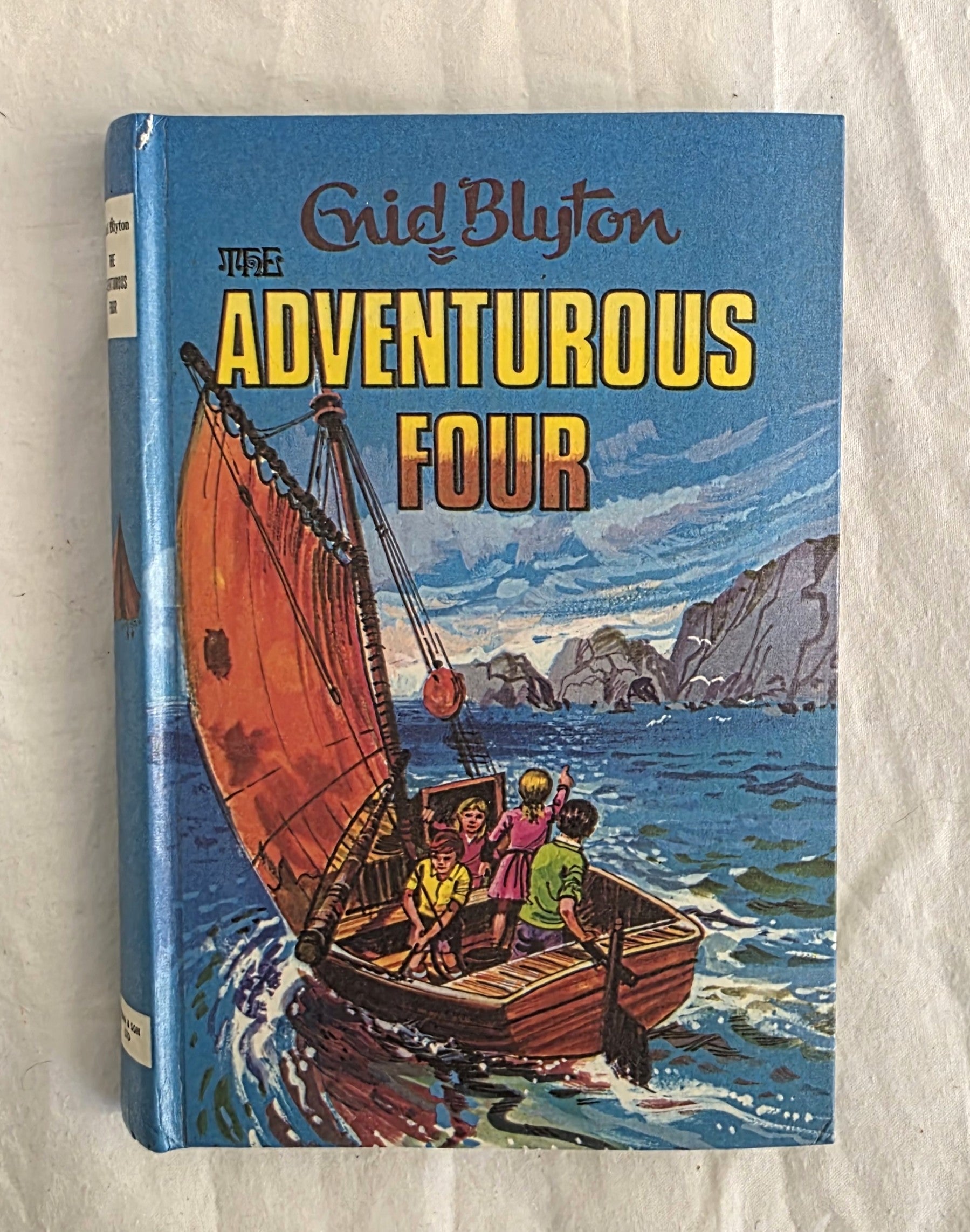 Book cover of 'Adventurous Four' by Enid Blyton with a boat and children illustration on a blue background.
