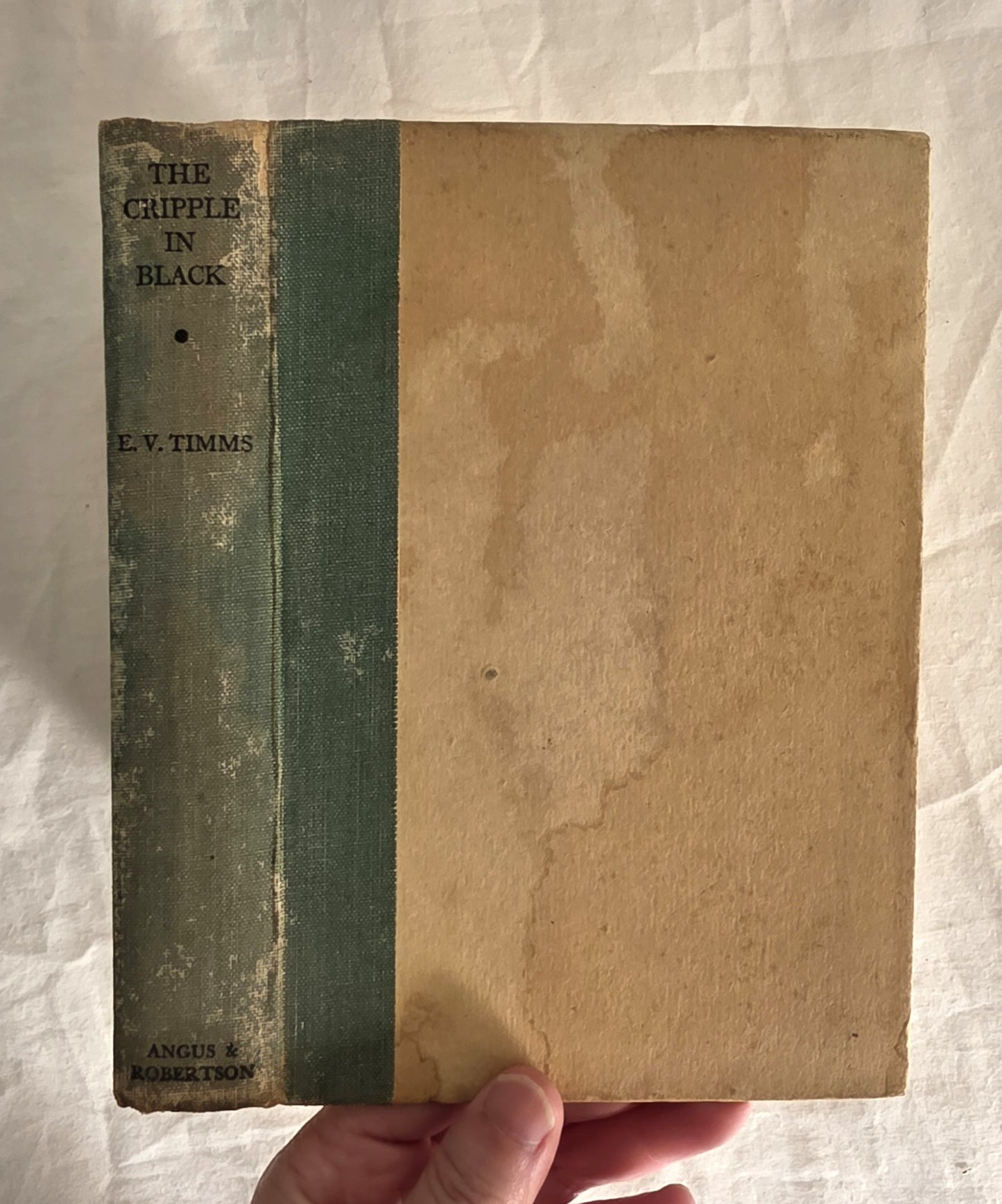 Vintage book titled 'The Cripple in Black' by E.V. Timms held against a textured white background.