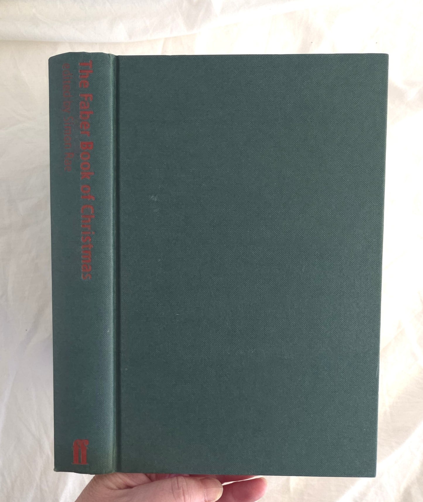 Green book titled 'The Faber Book of Christmas' held by a hand on a light background