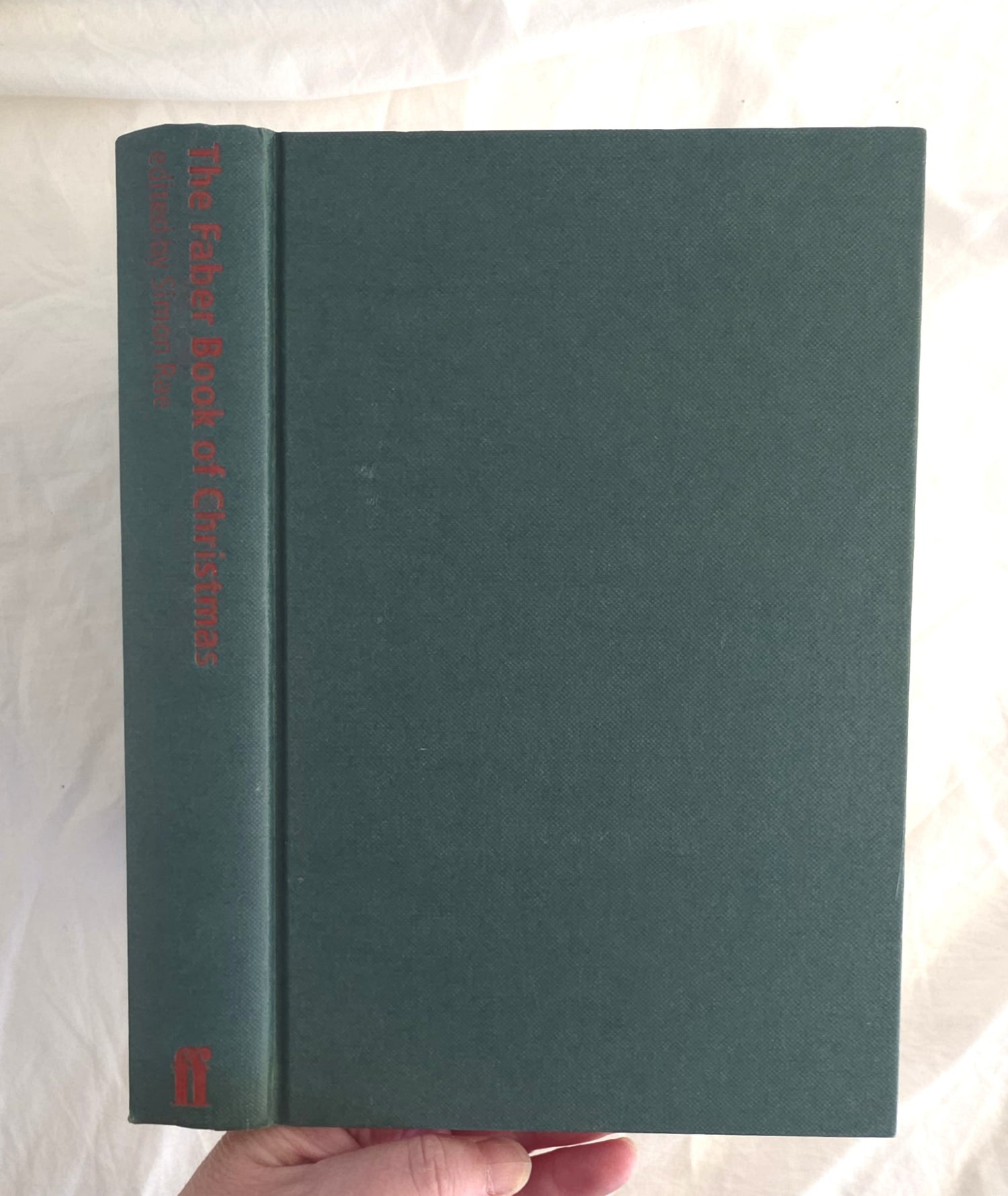 Green book titled 'The Faber Book of Christmas' held by a hand on a light background