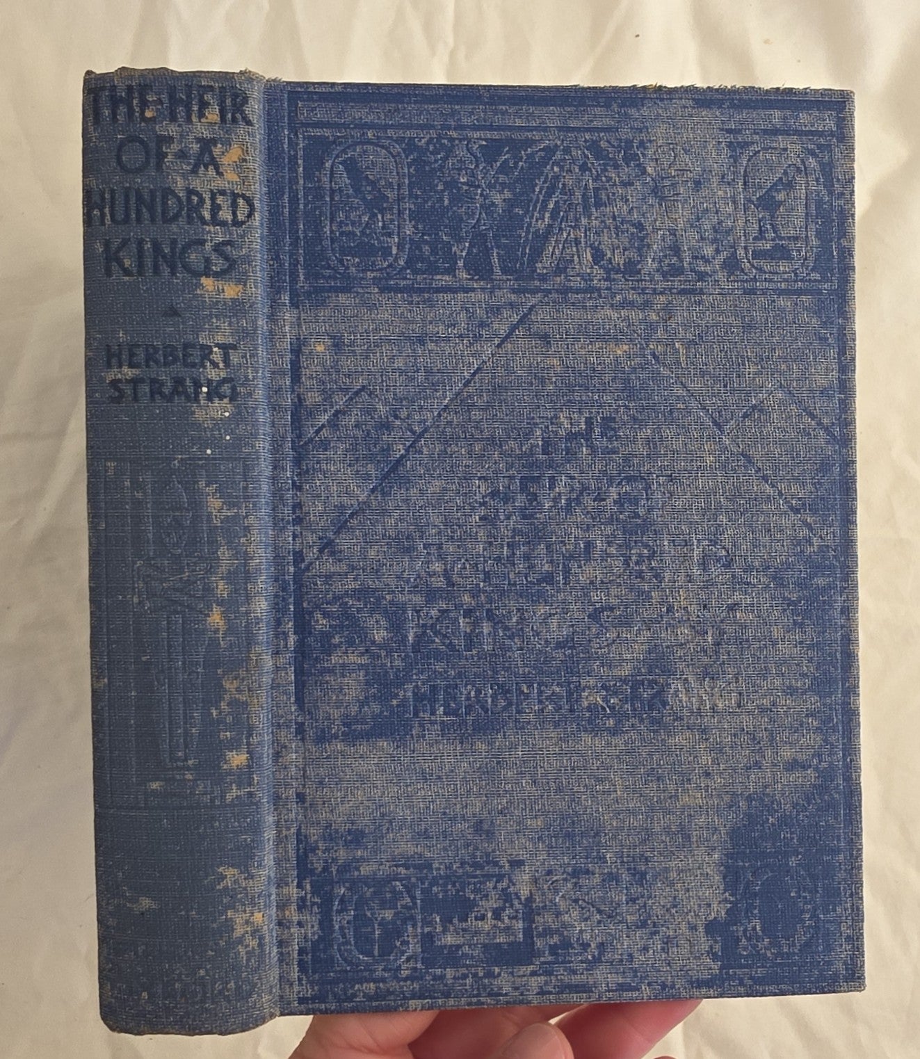 Vintage book titled 'The Heretic of a Hundred Kings' by Herbert Strang held in hand against a neutral background