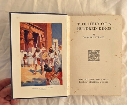 Open book titled 'The Heir of a Hundred Kings' by Herbert Strang, held against a neutral background.