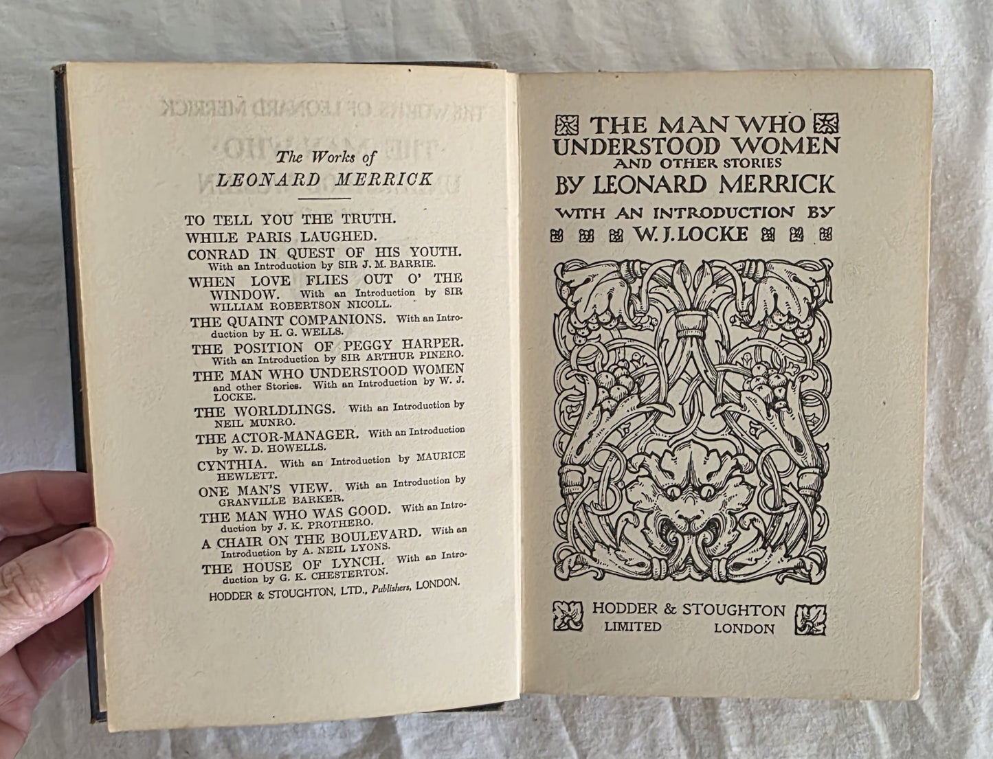 Open book with decorative text and title page held by a hand on a light background