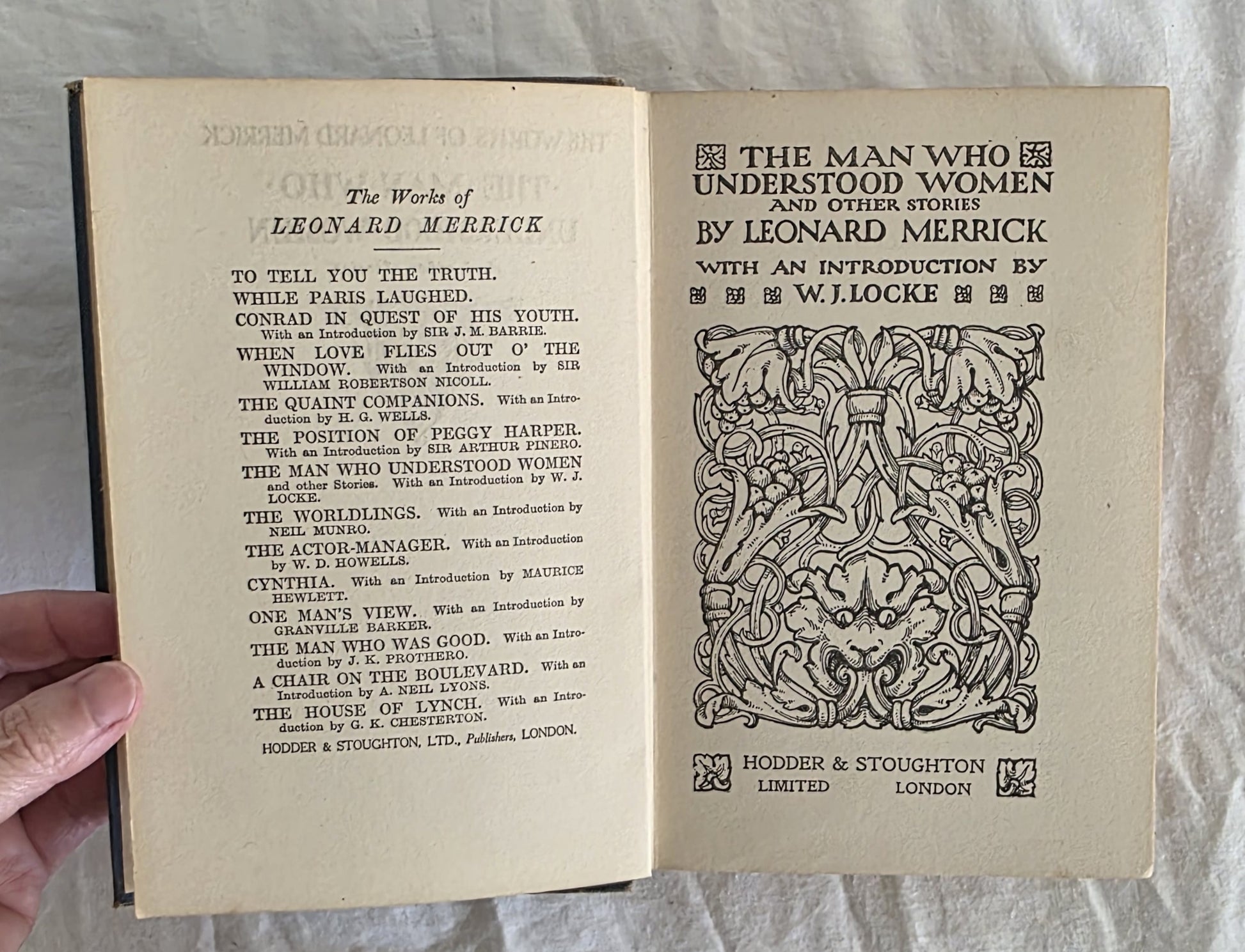 Open book with decorative text and title page held by a hand on a light background