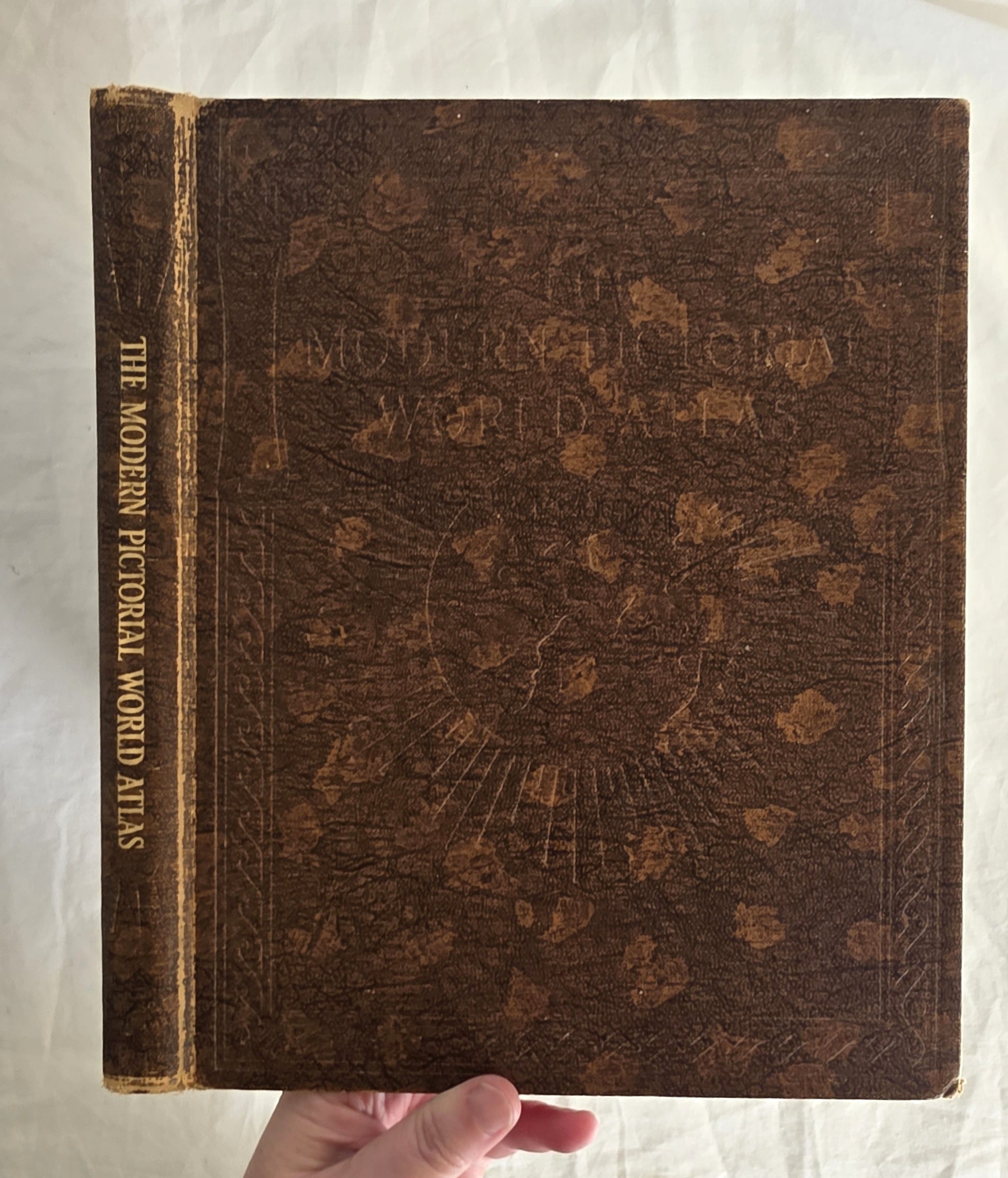 Vintage atlas with decorative cover held by a hand on a white background