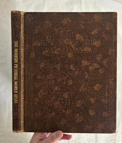 Vintage atlas with decorative cover held by a hand on a white background