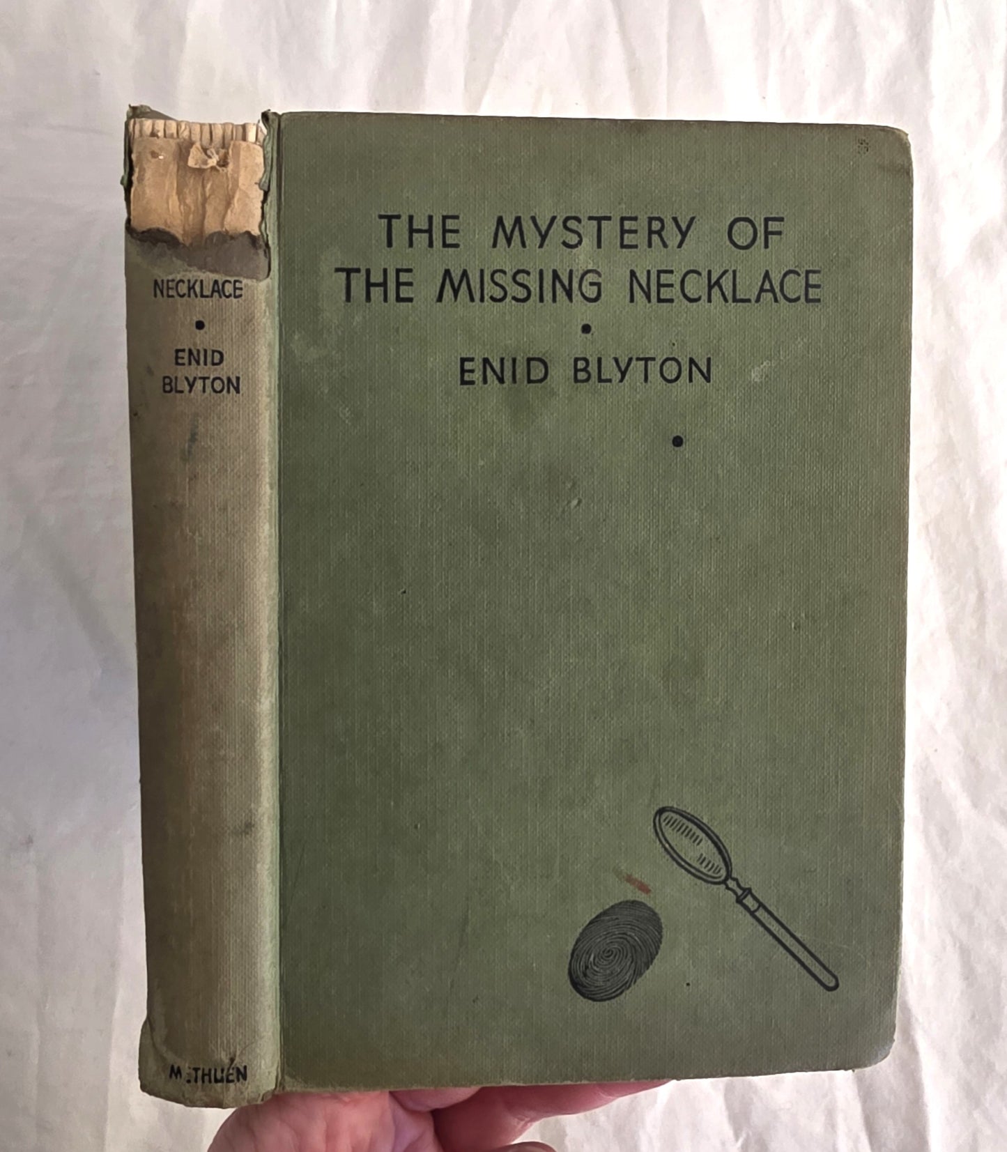 Vintage book titled 'The Mystery of the Missing Necklace' by Enid Blyton held against a white background.