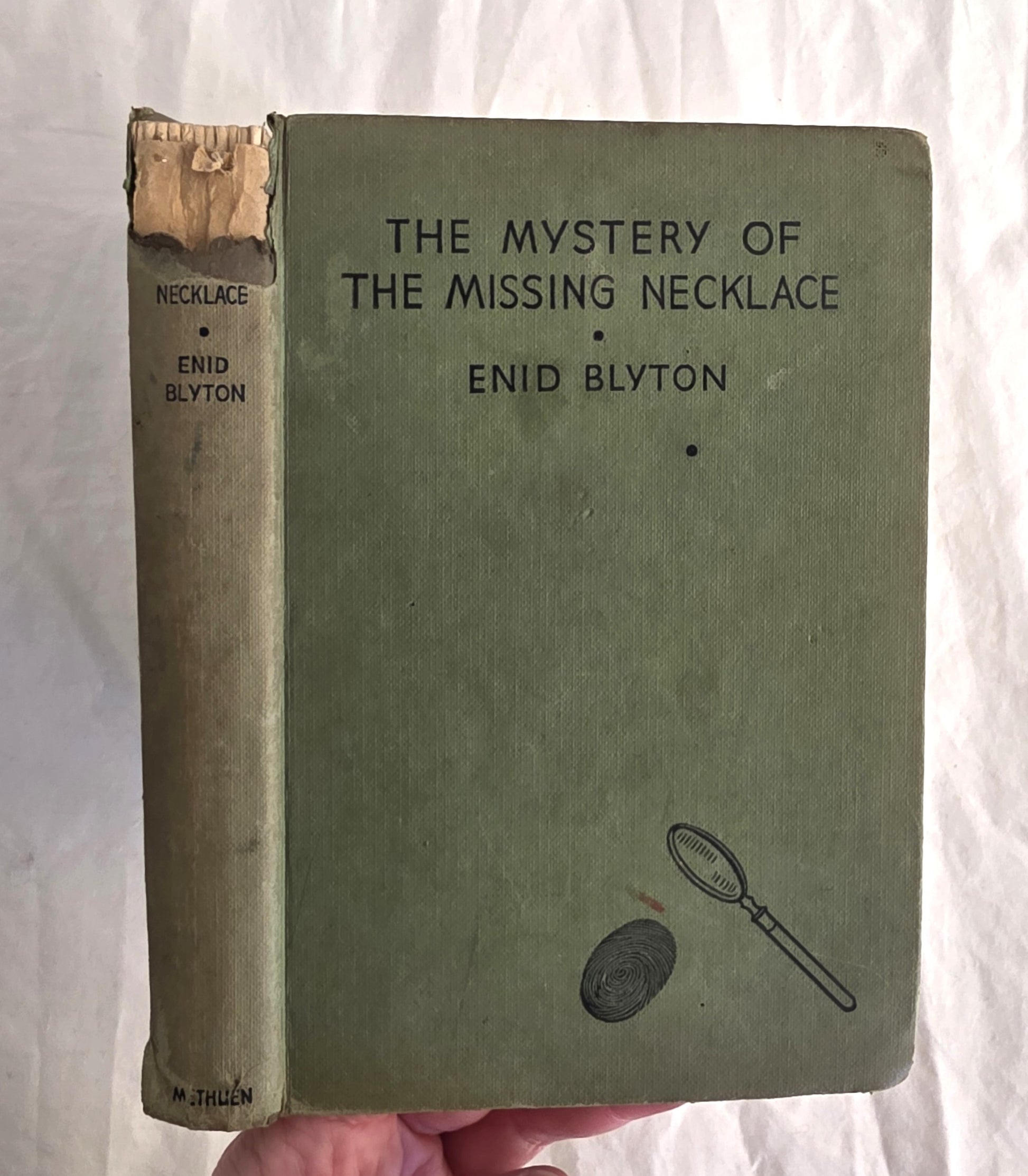 Vintage book titled 'The Mystery of the Missing Necklace' by Enid Blyton held against a white background.