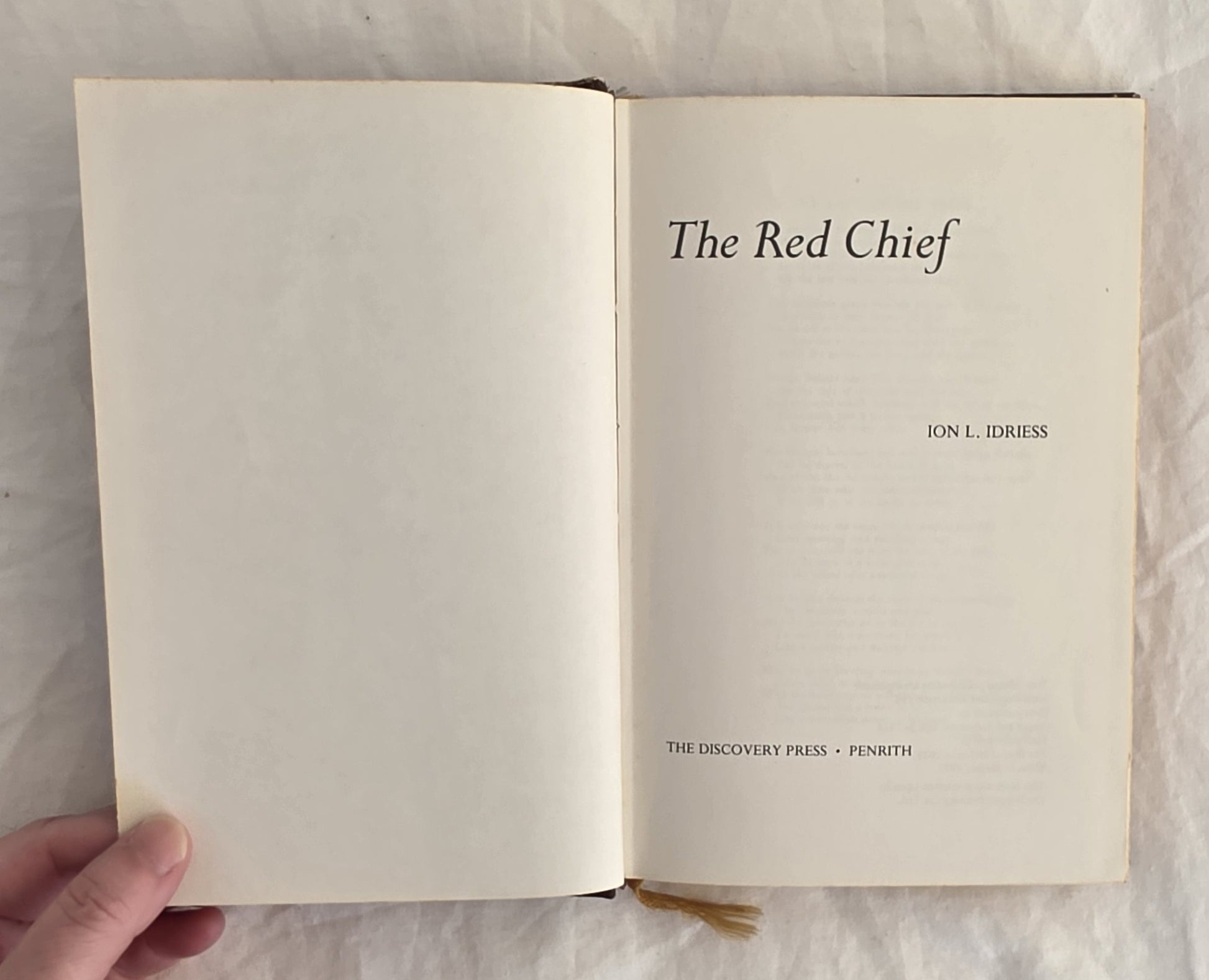 Open book titled 'The Red Chief' by Ion L. Idriess held by a hand on a textured surface.