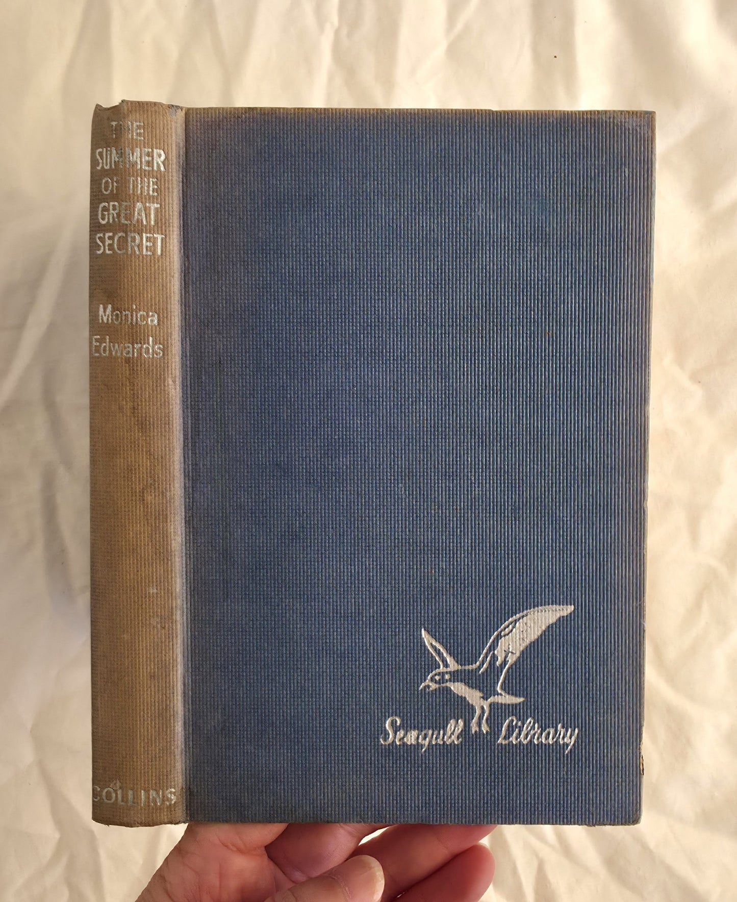 Blue book with 'Seagull Library' logo held by a hand on a white background