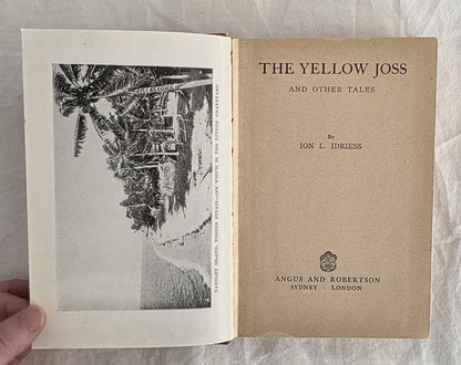 Open book titled 'The Yellow Joss and Other Tales' by Ion L. Idriess, held against a textured gray background.