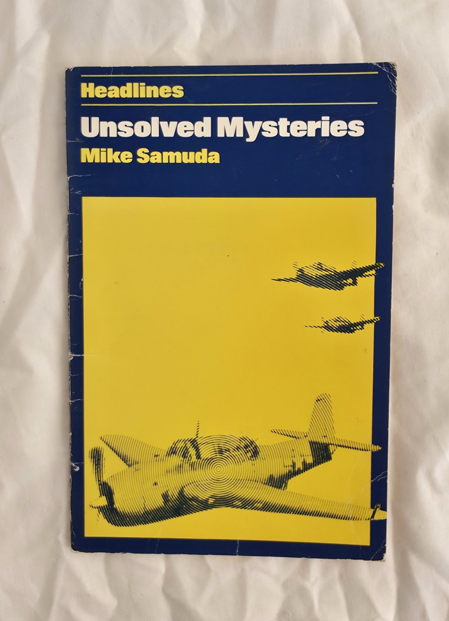 Book titled 'Unsolved Mysteries' by Mike Samuda with airplane illustration on a yellow background