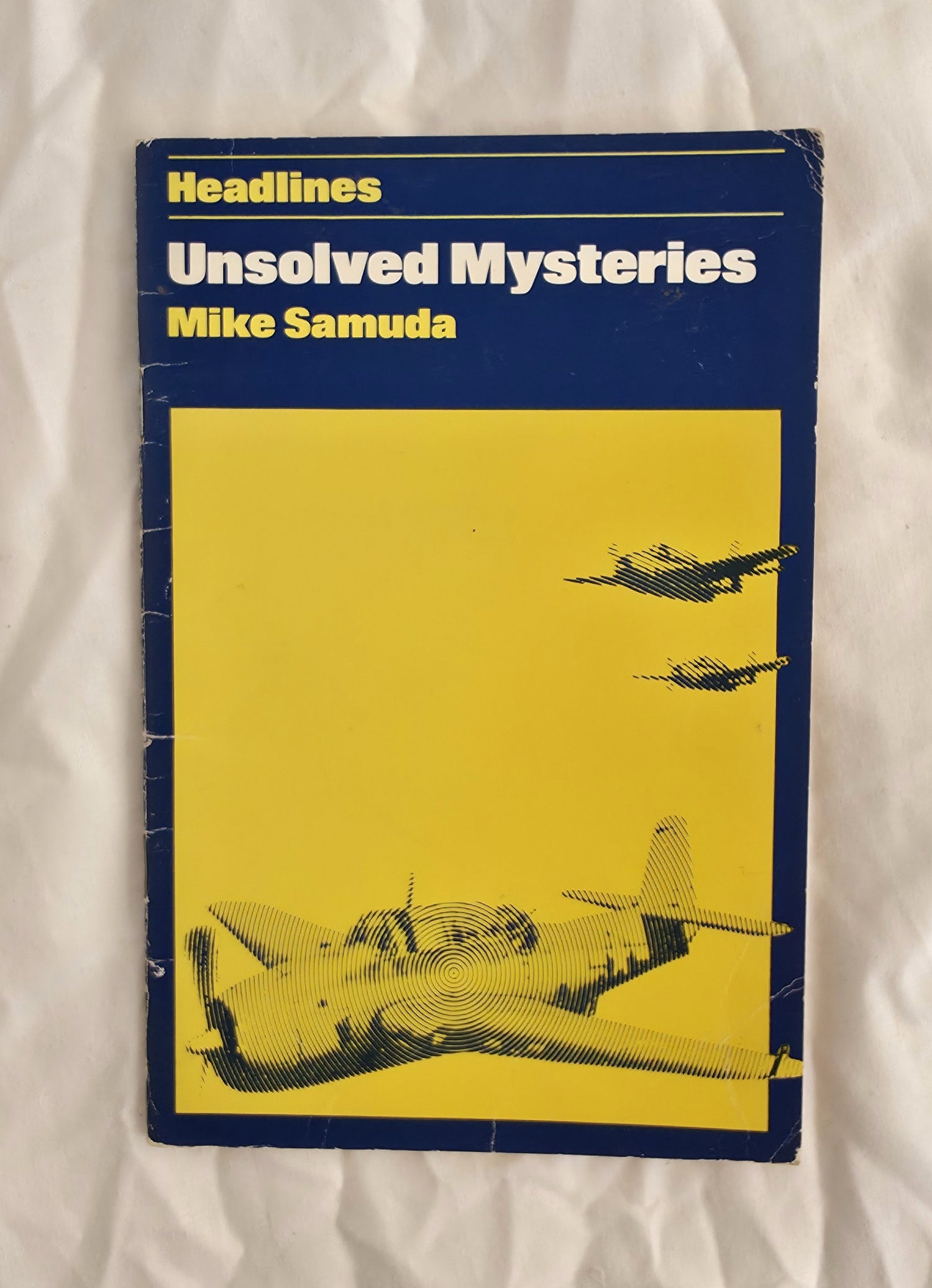 Book titled 'Unsolved Mysteries' by Mike Samuda with airplane illustration on a yellow background
