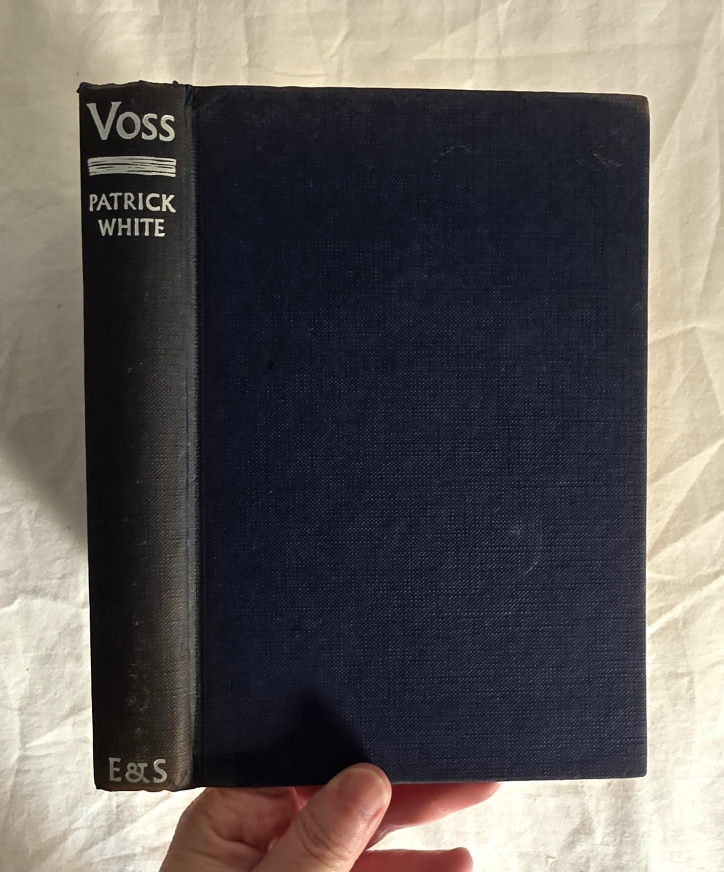 Black book titled 'Voss' by Patrick White held against a textured white background